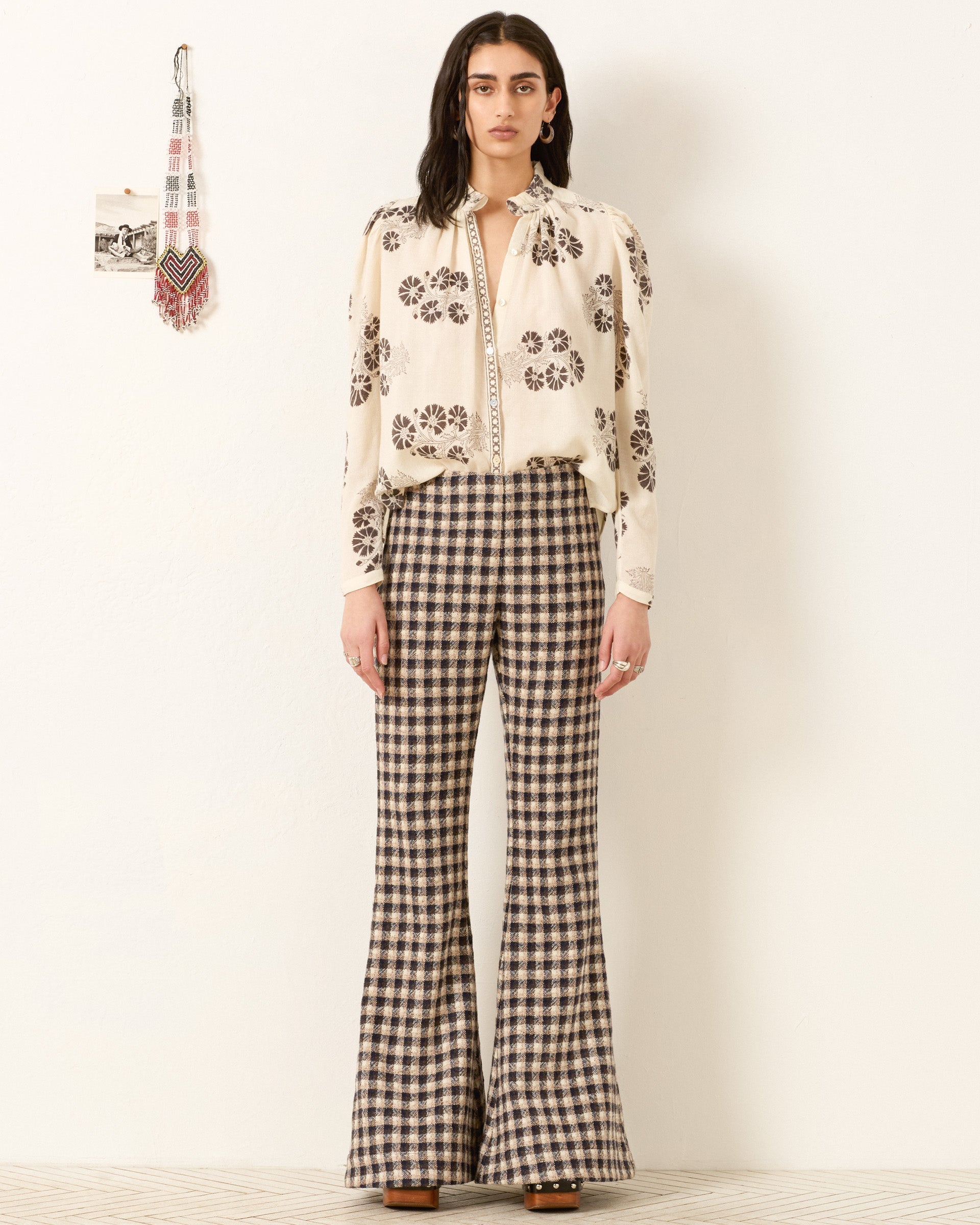 Model wearing white floral print blouse with decorative trim and checkered flare pants