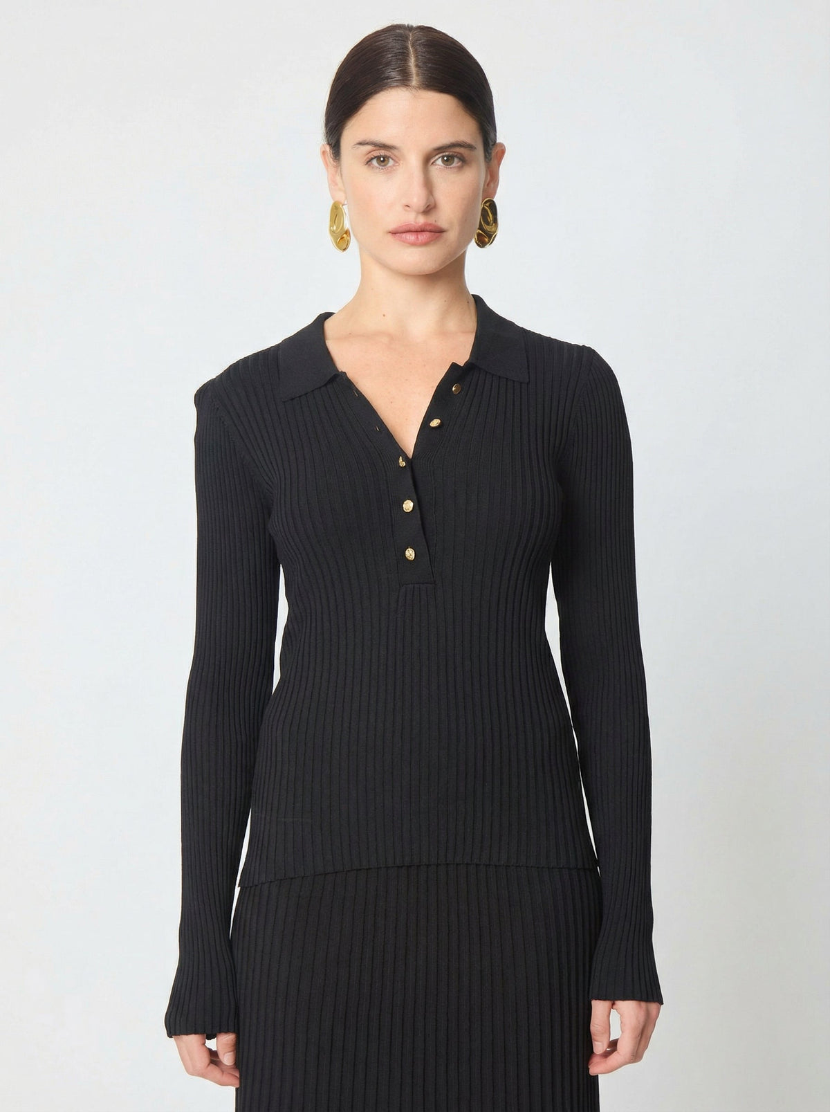 Model wearing black ribbed knit polo top with gold buttons and long sleeves