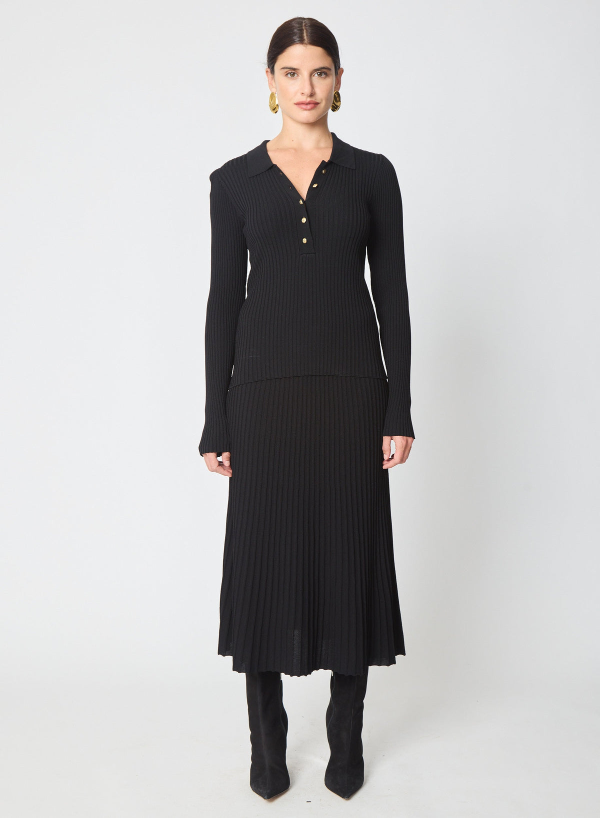 Model wearing black ribbed knit polo top with long sleeves and gold button detail