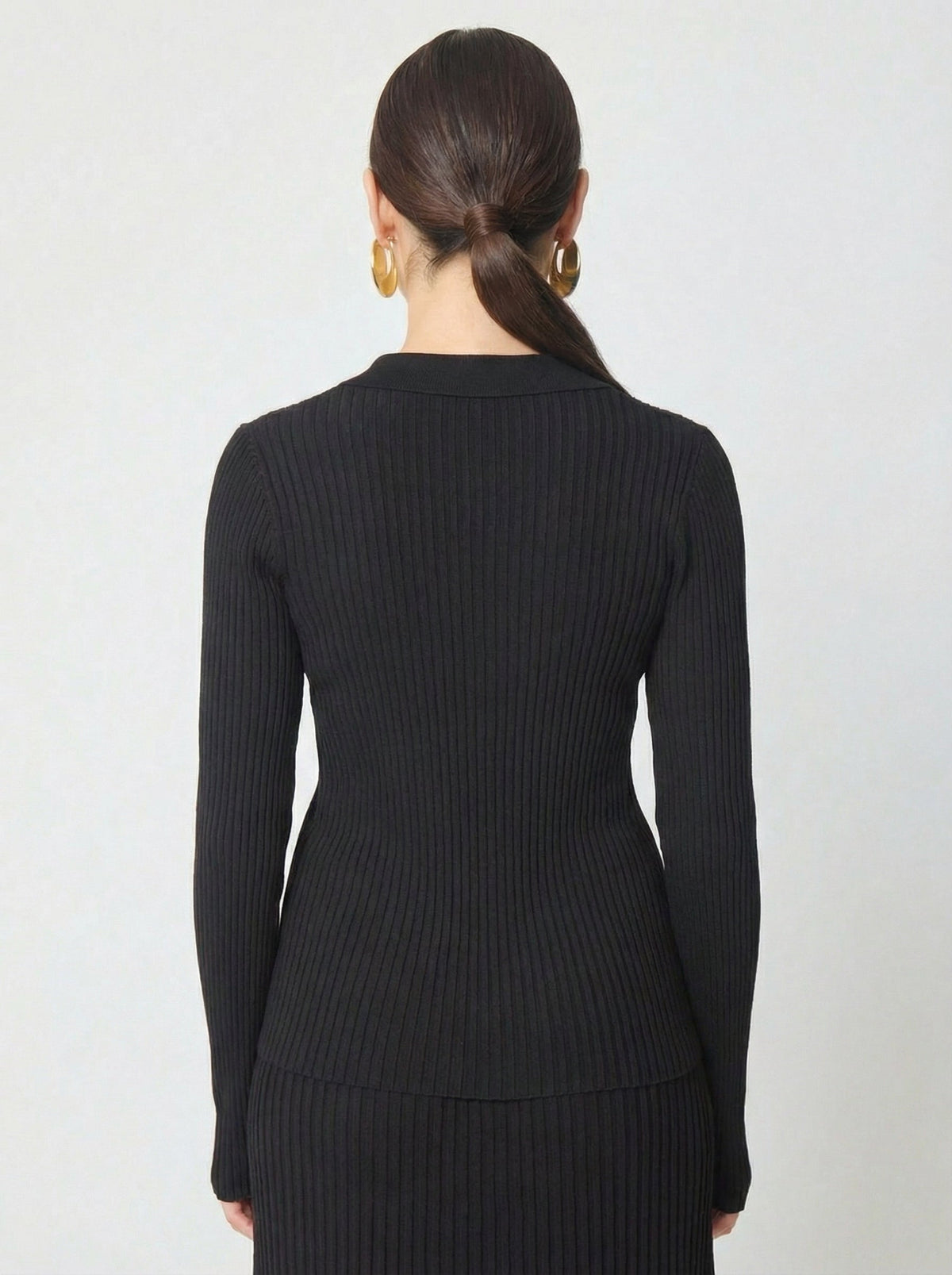 Back view of black ribbed knit long-sleeve polo top worn by model with low ponytail