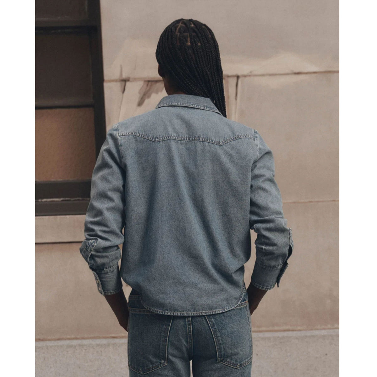 Model wearing The GREAT Howdy Top in Oldham Wash denim, back view with braids