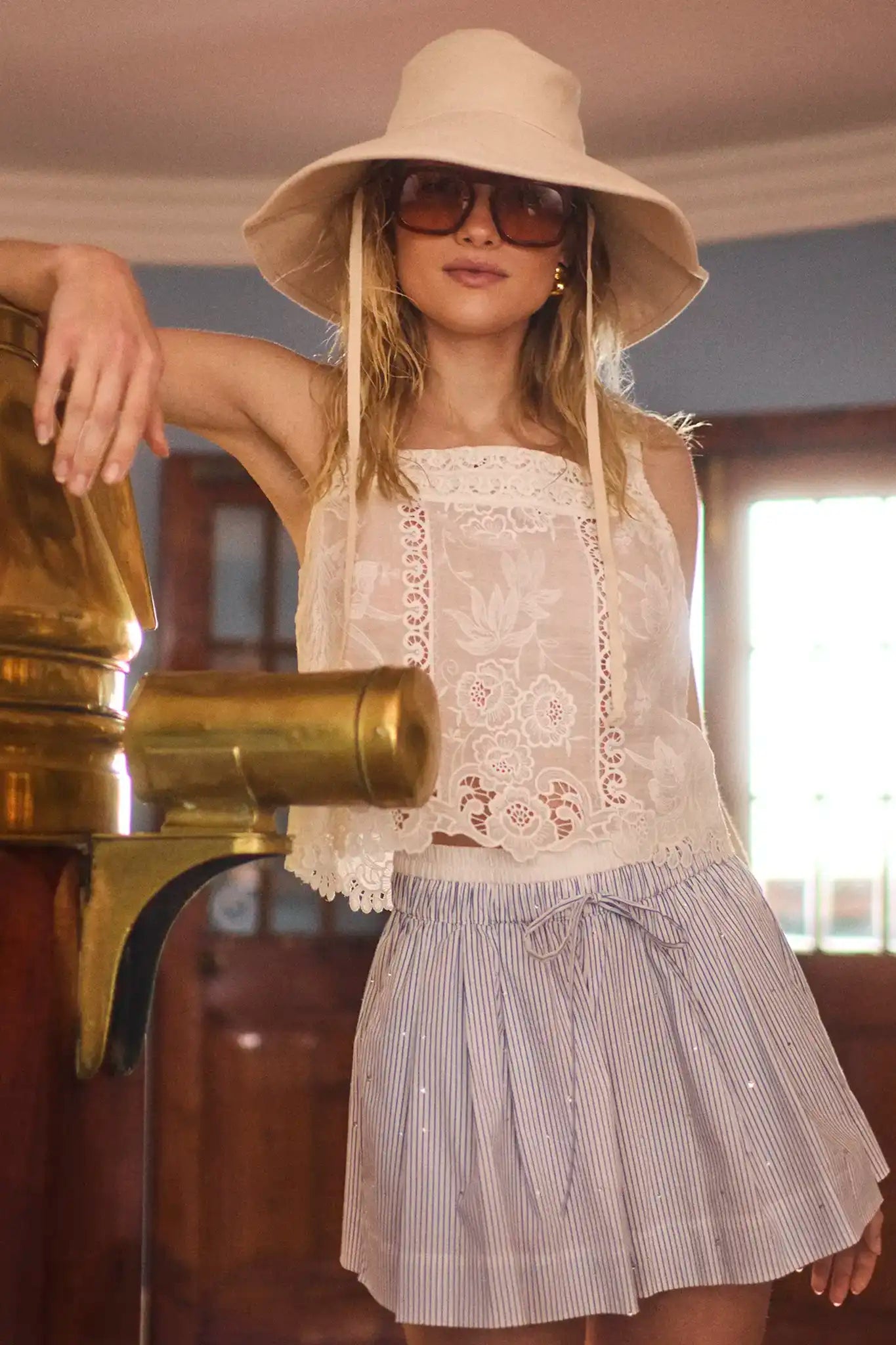Woman wearing white lace eyelet top with wide-brimmed hat and striped shorts in lifestyle setting