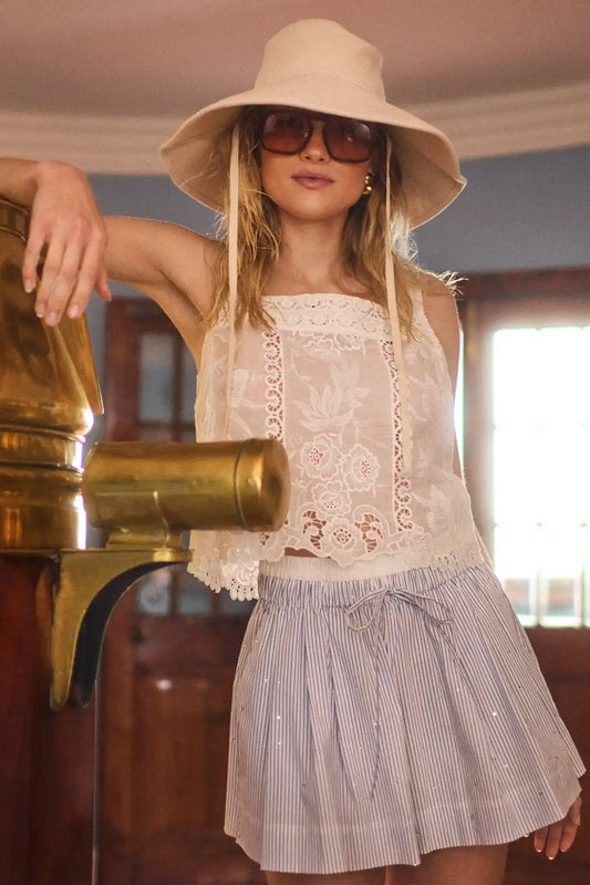 Woman wearing white lace eyelet top with wide-brimmed hat and striped shorts in lifestyle setting
