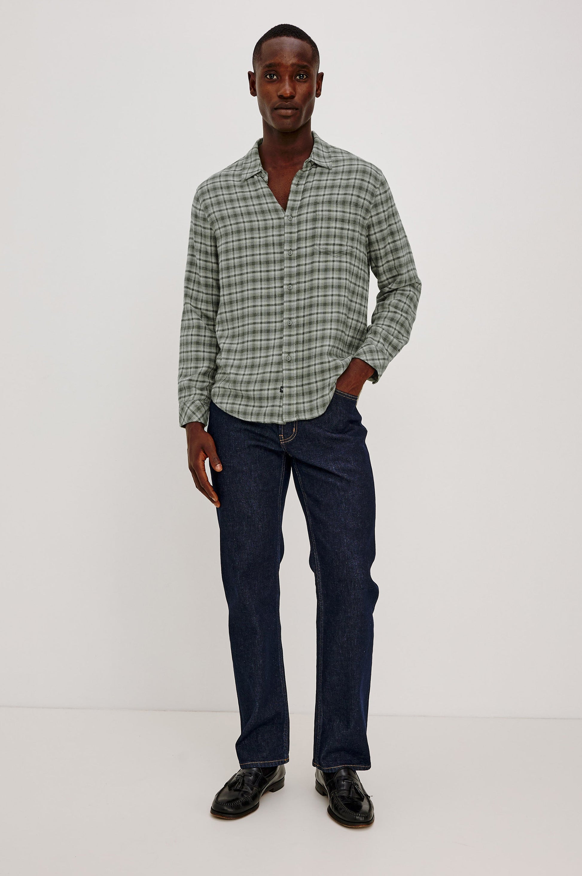 Male model wearing Rails Lennox long sleeve plaid shirt in sage green birch forest with dark jeans