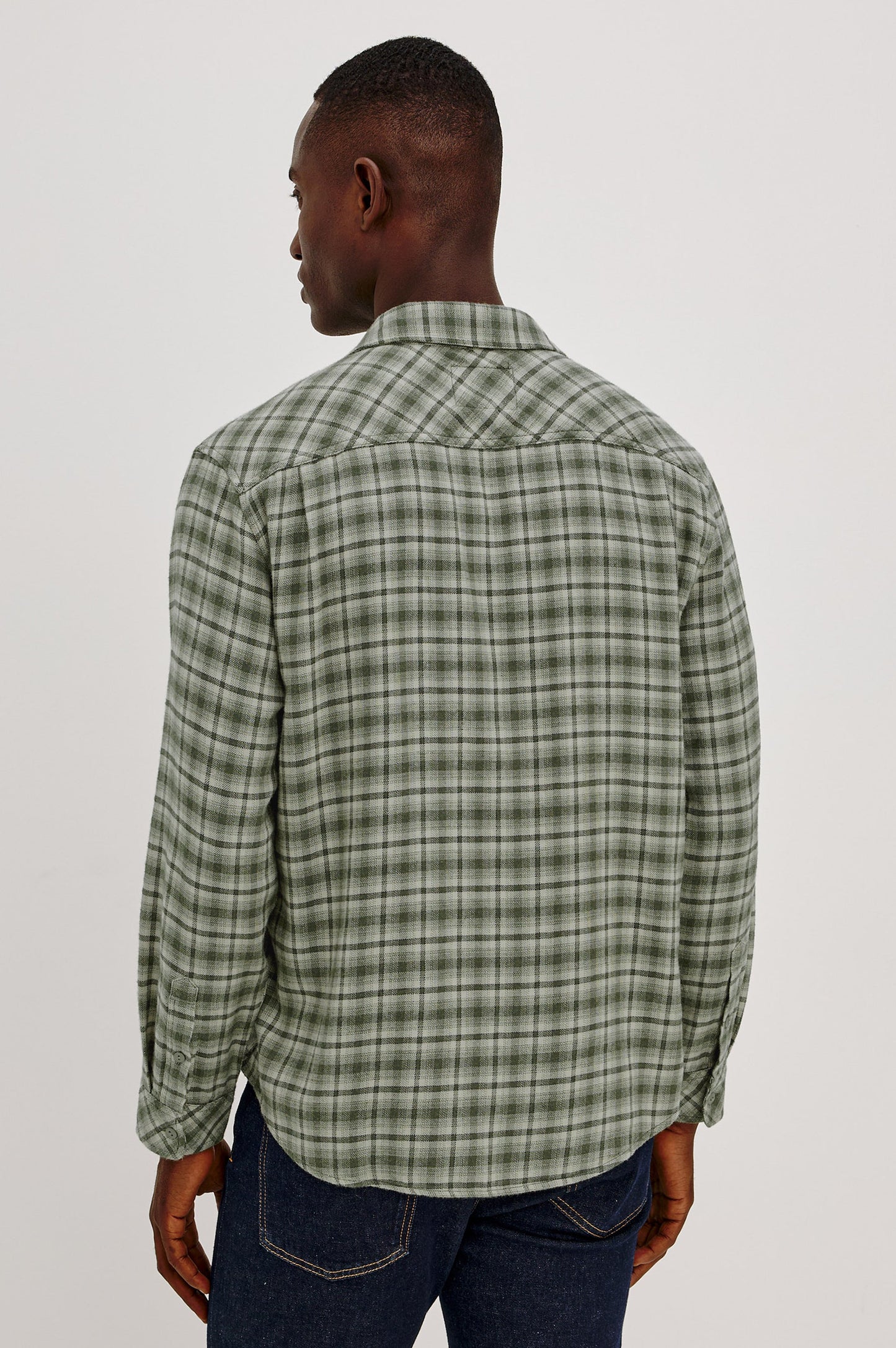 Back view of male model wearing green plaid flannel shirt with dark jeans