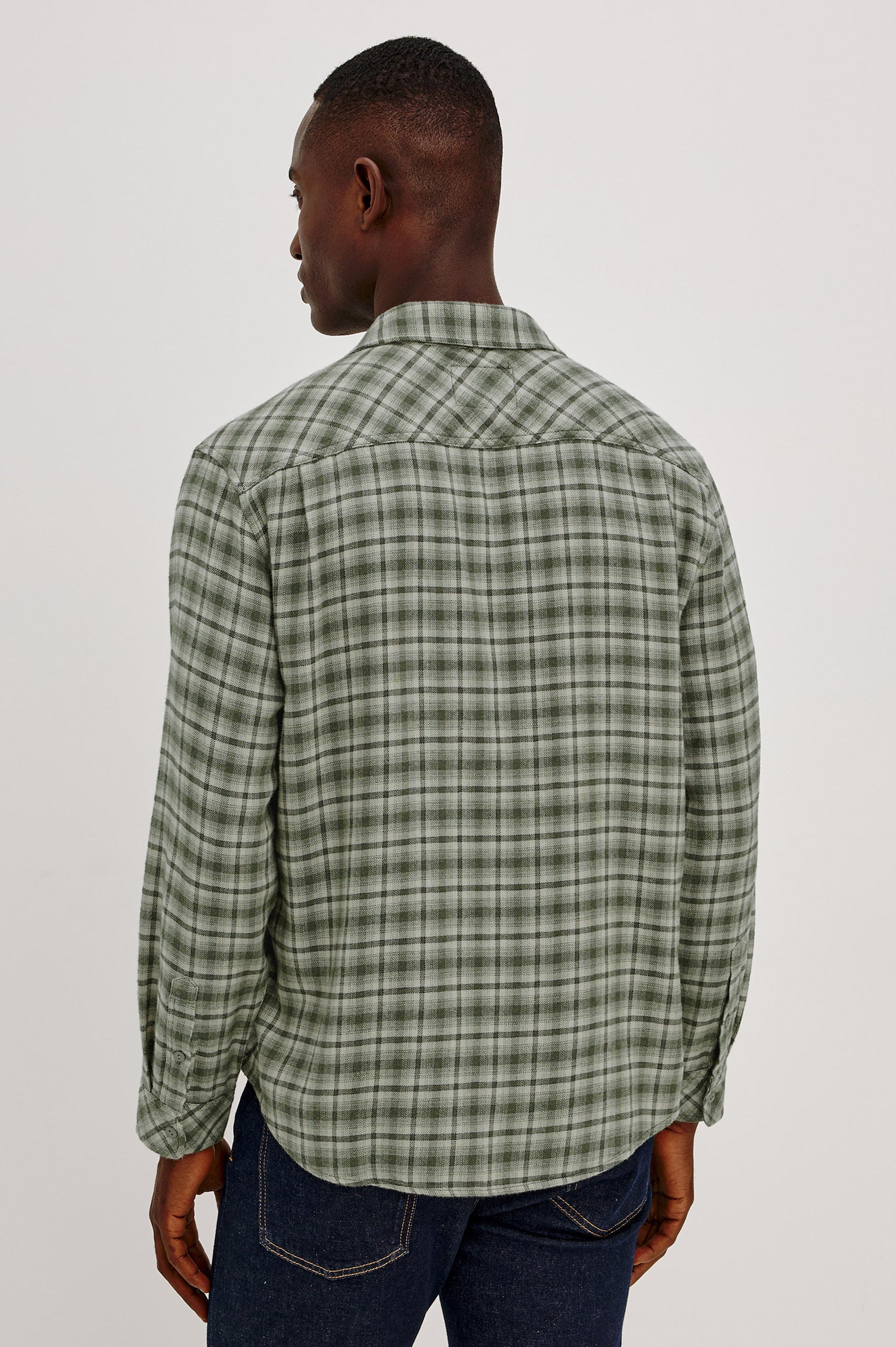 Back view of male model wearing green plaid flannel shirt with dark jeans
