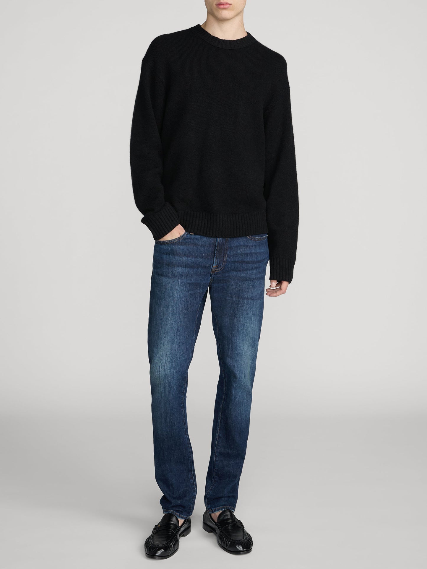 Male model wearing Frame L'Homme Slim jeans in mid blue wash with black sweater