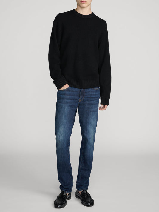 Male model wearing Frame L'Homme Slim jeans in mid blue wash with black sweater