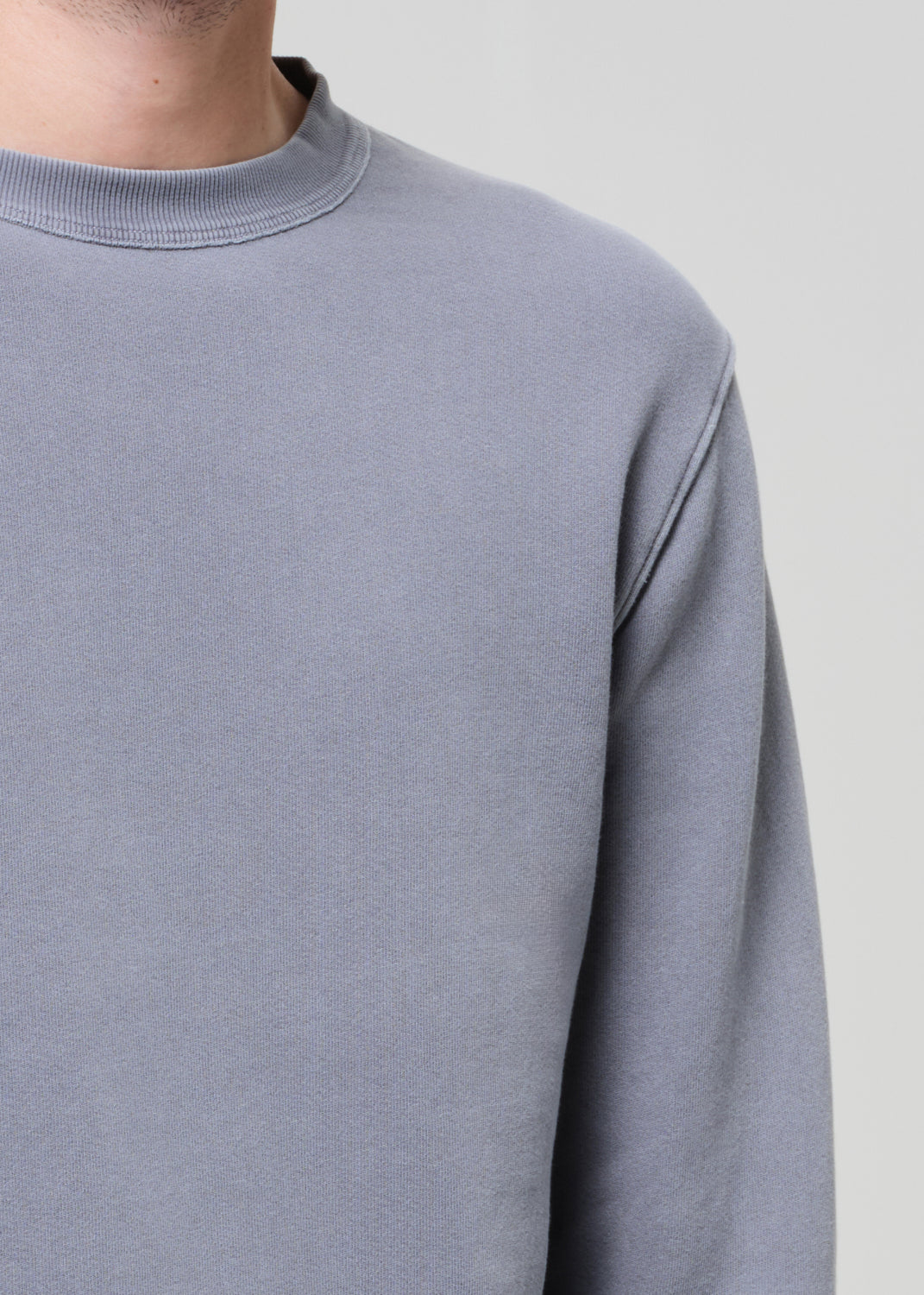 Close-up of a man wearing a grey-blue crewneck sweatshirt with ribbed collar