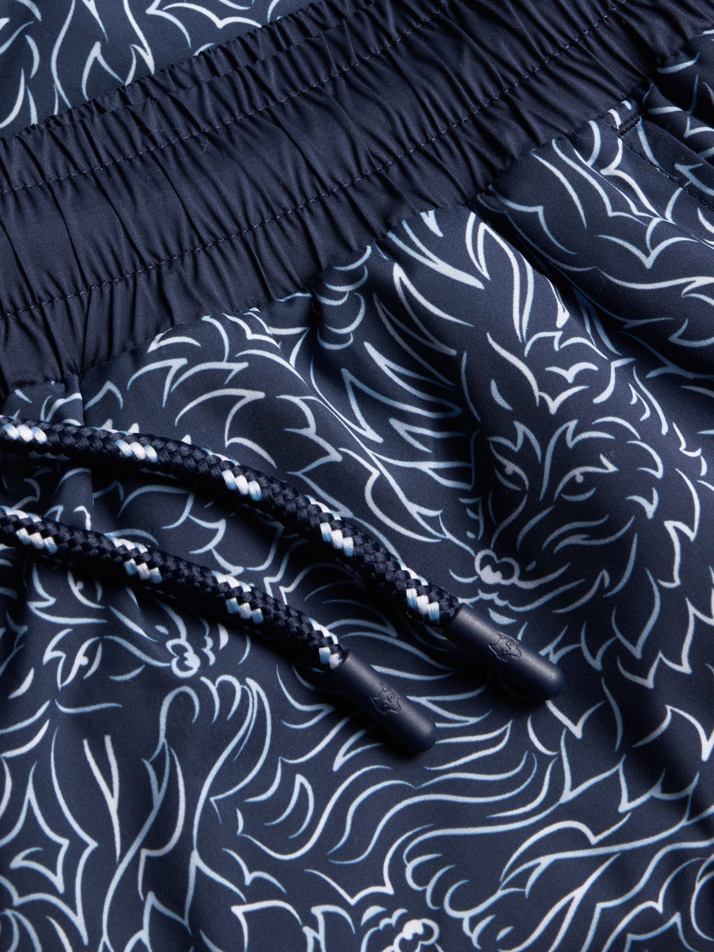 Close-up detail of navy blue swim shorts with white wave pattern and drawstring
