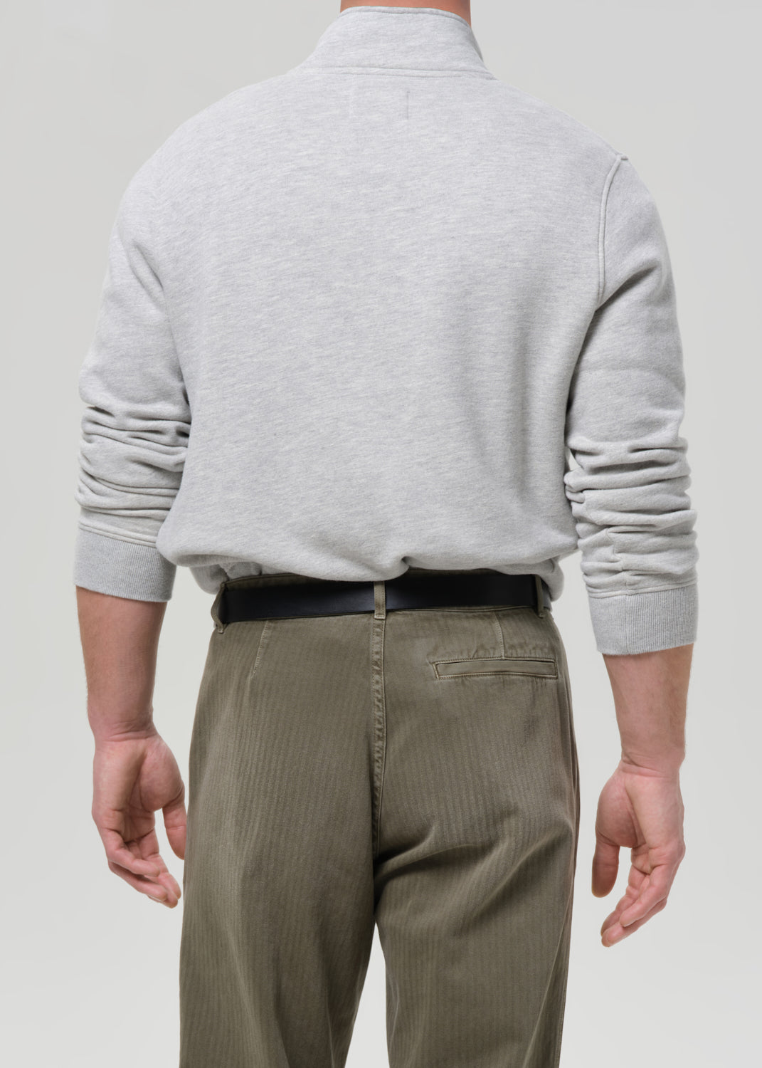 Back view of male model wearing heather grey half-button pullover sweatshirt with olive trousers
