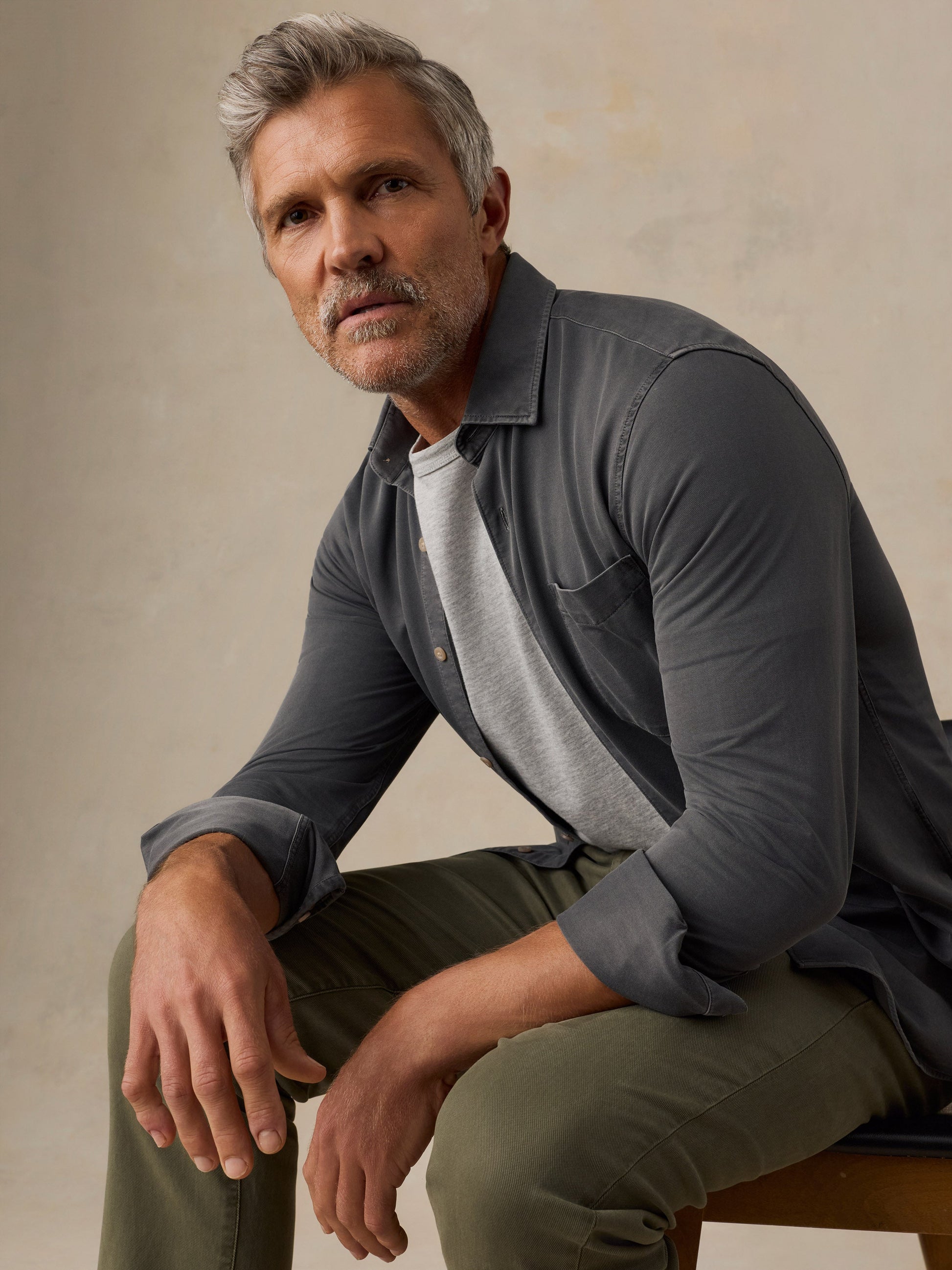 Male model seated wearing Faherty Costa Piqué Shirt in dark charcoal Ridge Black over gray tee