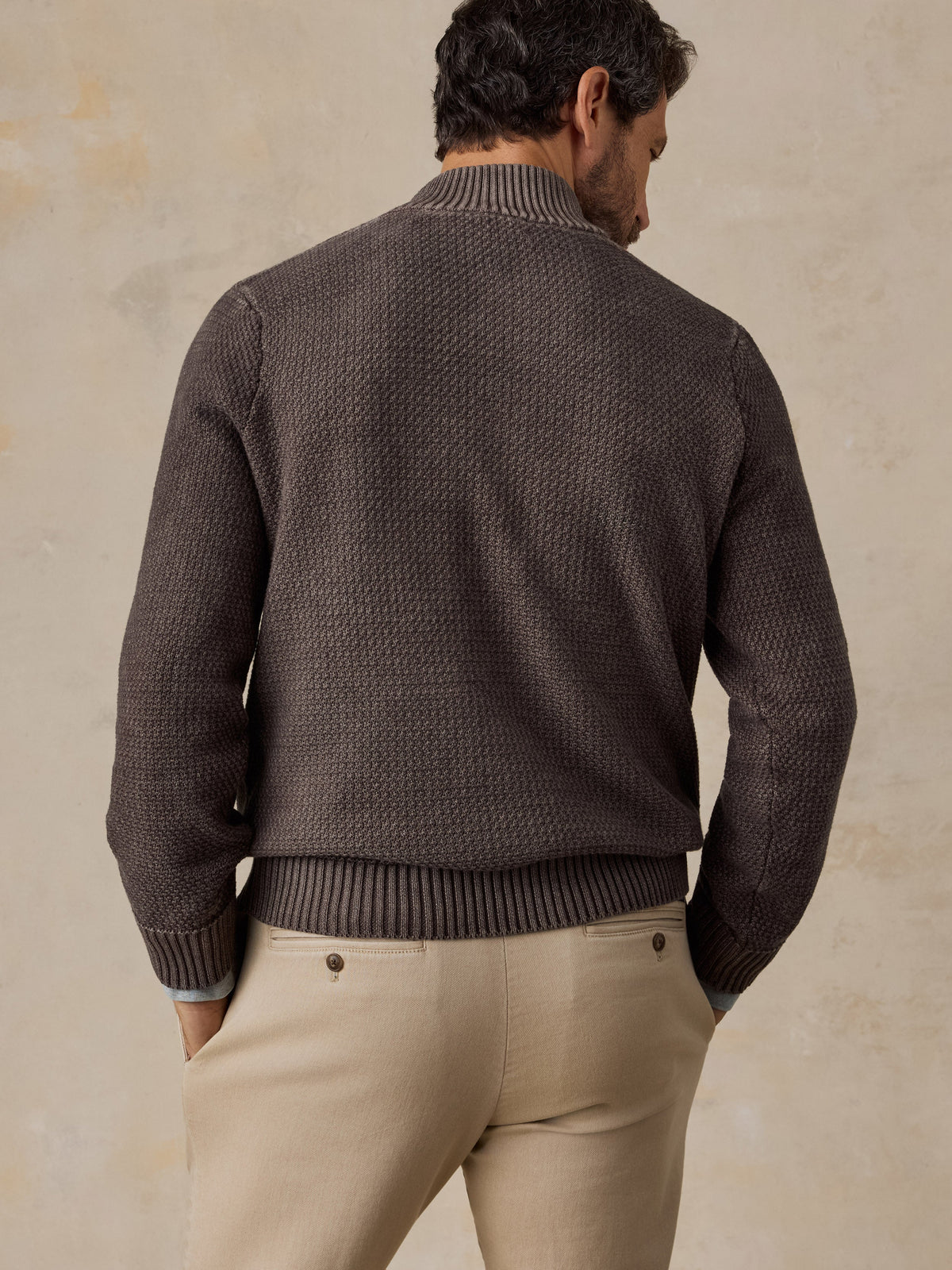 Back view of man wearing brown textured quarter-button knit sweater with ribbed collar and hem