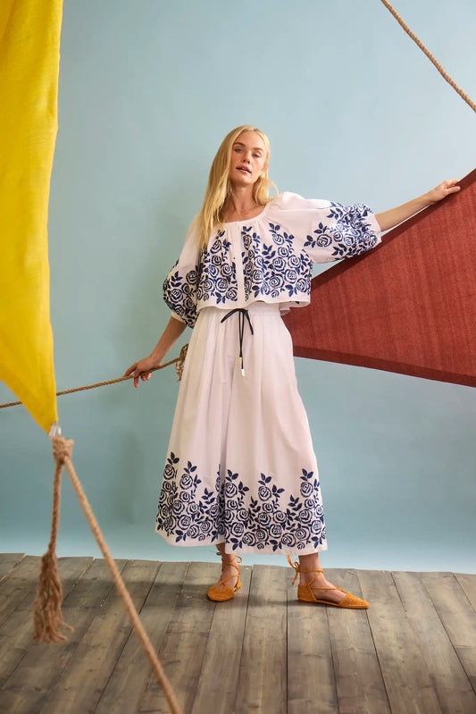 Model wearing white embroidered top with blue rose pattern and matching skirt in nautical styled photoshoot