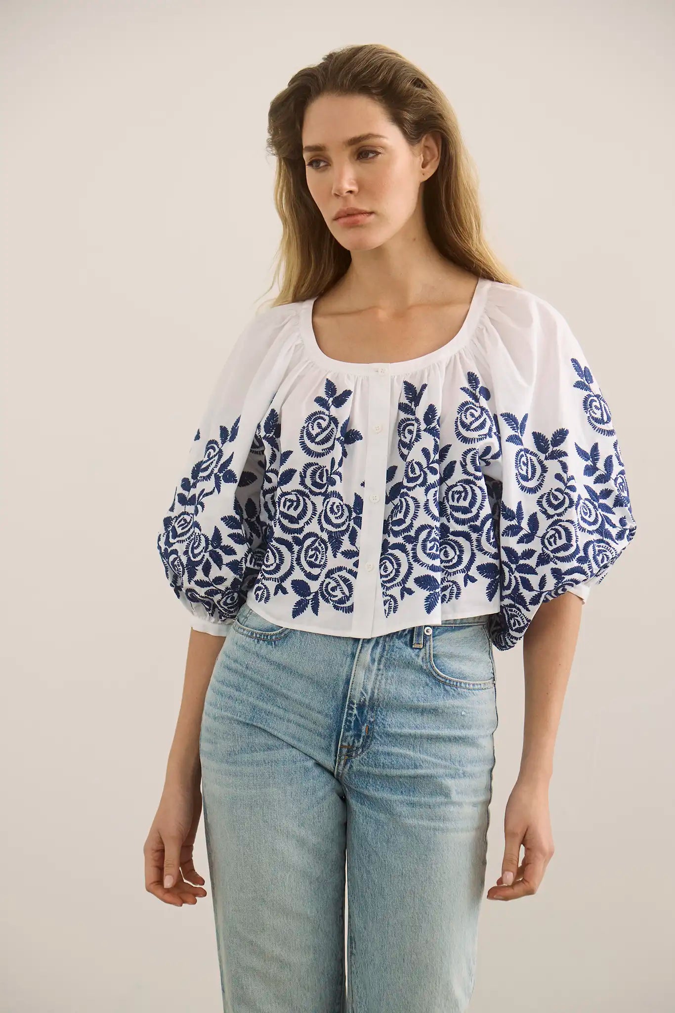 Woman wearing white peasant blouse with blue embroidered rose pattern and light wash jeans