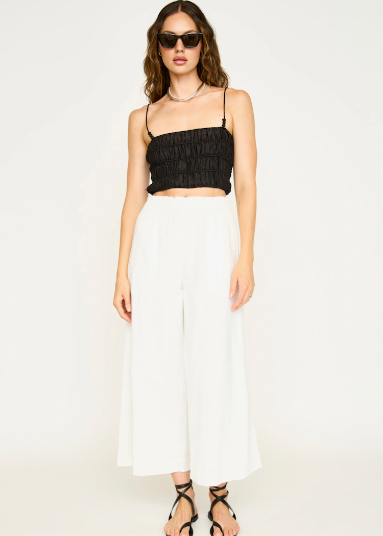Model wearing white wide-leg cropped pants with black ruched crop top and sunglasses