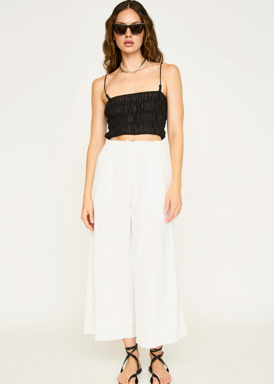 Model wearing white wide-leg cropped pants with black ruched crop top and sunglasses