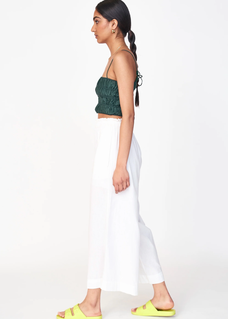 Woman wearing white wide-leg pants with green ruched top in studio setting
