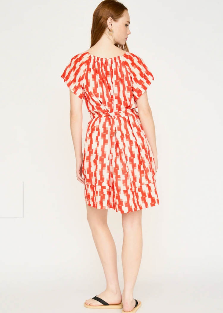 Woman wearing red and white patterned short dress with flutter sleeves and belt, back view