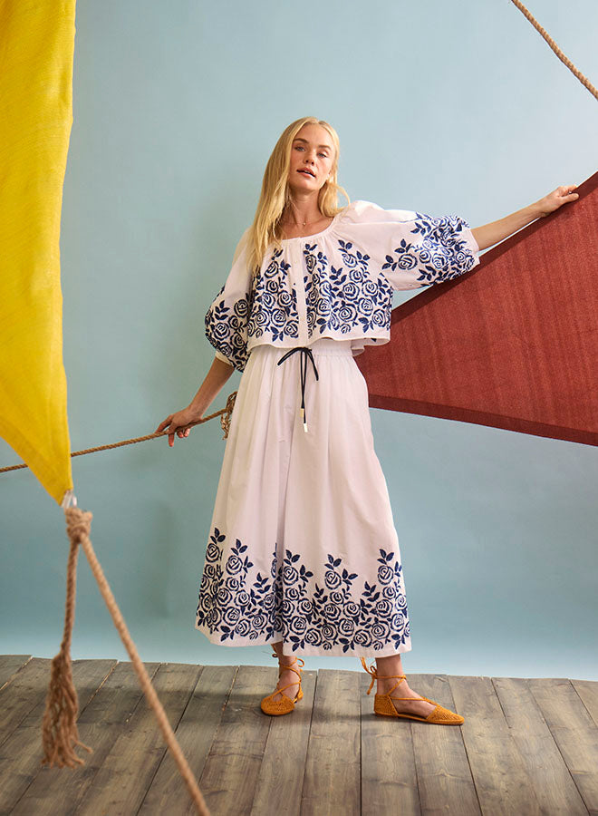 Woman wearing white embroidered two-piece set with blue floral patterns in styled photo