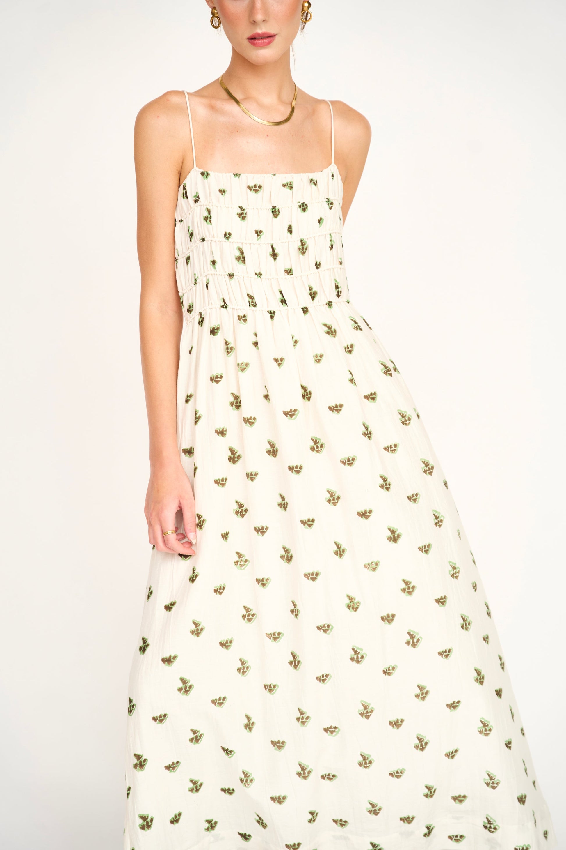 Woman wearing cream colored midi dress with green floral print and thin straps