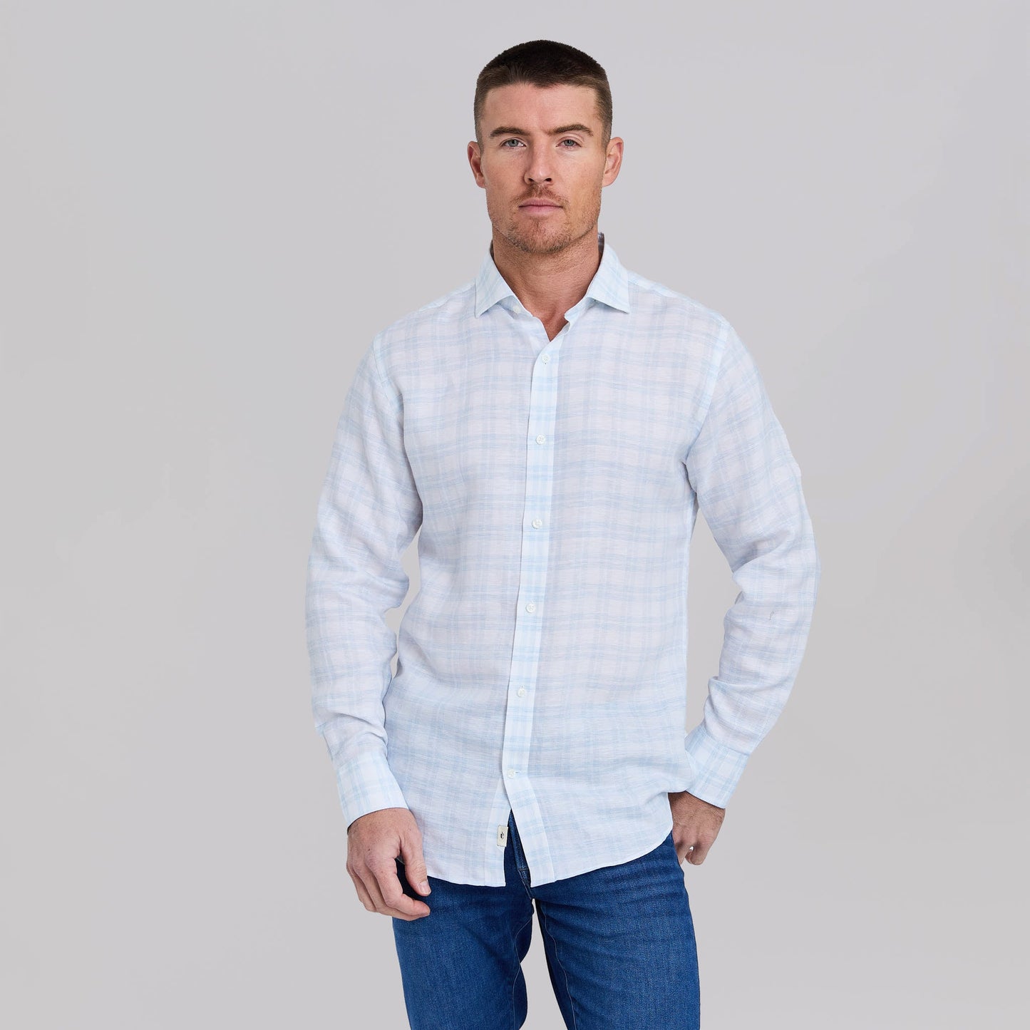 Man wearing white button-up shirt with light blue plaid pattern and dark jeans