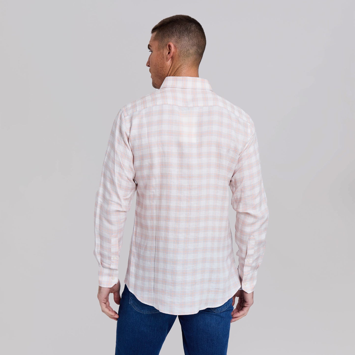 Man wearing light pink and white gingham plaid button-down shirt with jeans, back view