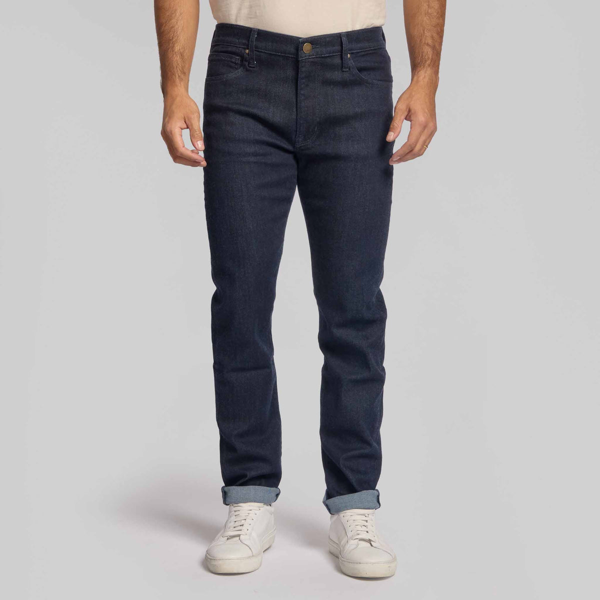 Man wearing dark indigo 4-way stretch jeans with white sneakers and cuffed hem