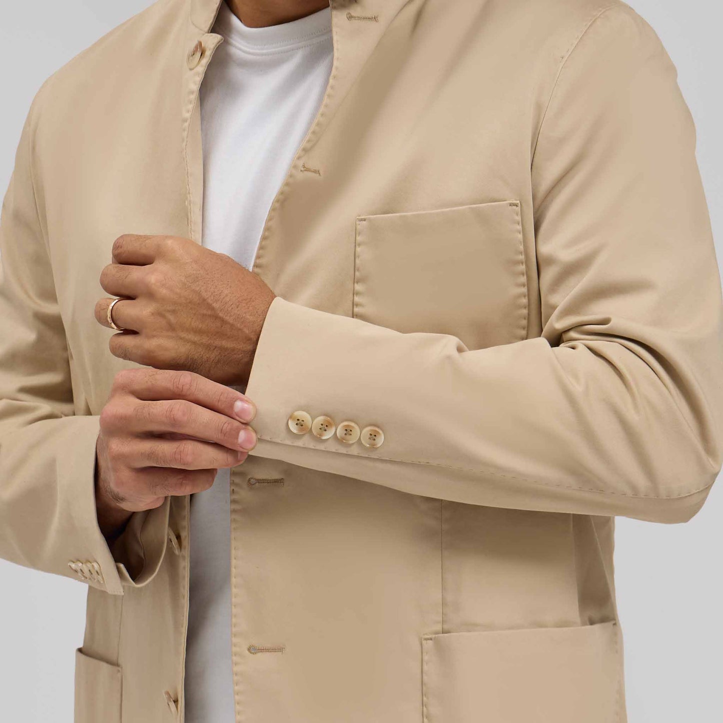 Close-up of tan mandarin collar jacket with five sleeve buttons worn over white tee