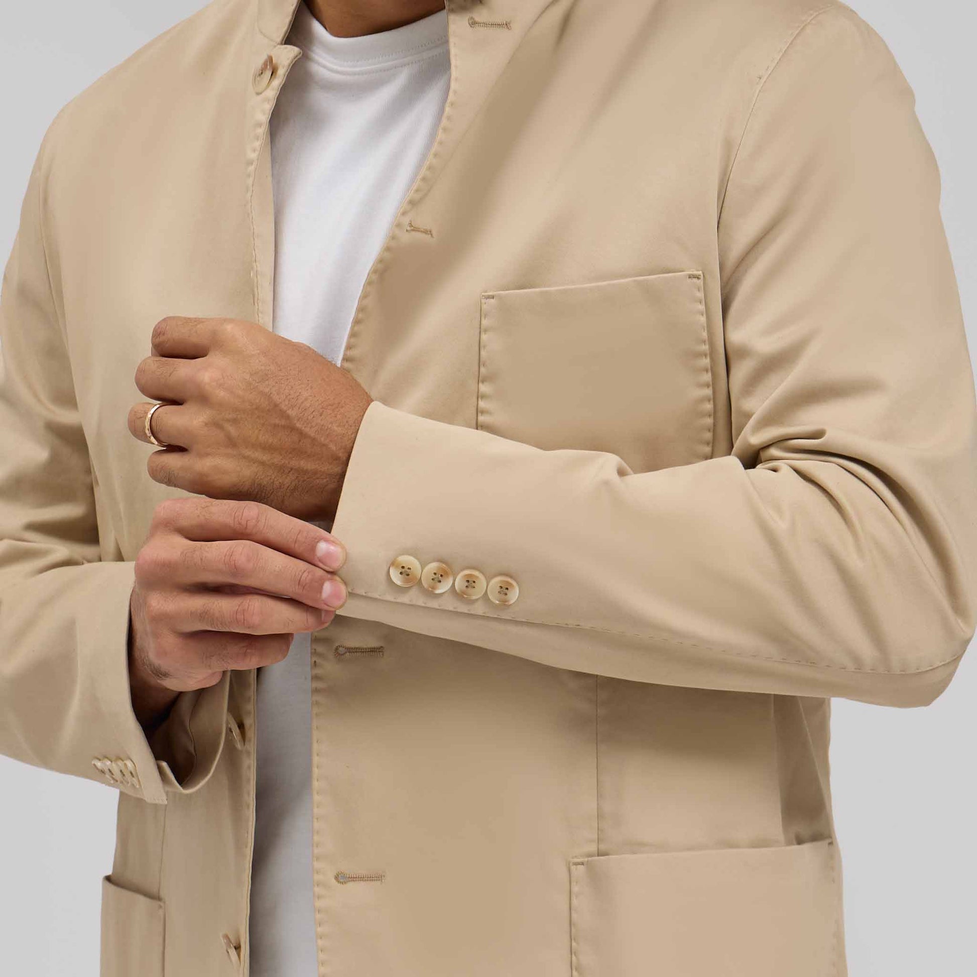 Close-up of tan mandarin collar jacket with five sleeve buttons worn over white tee