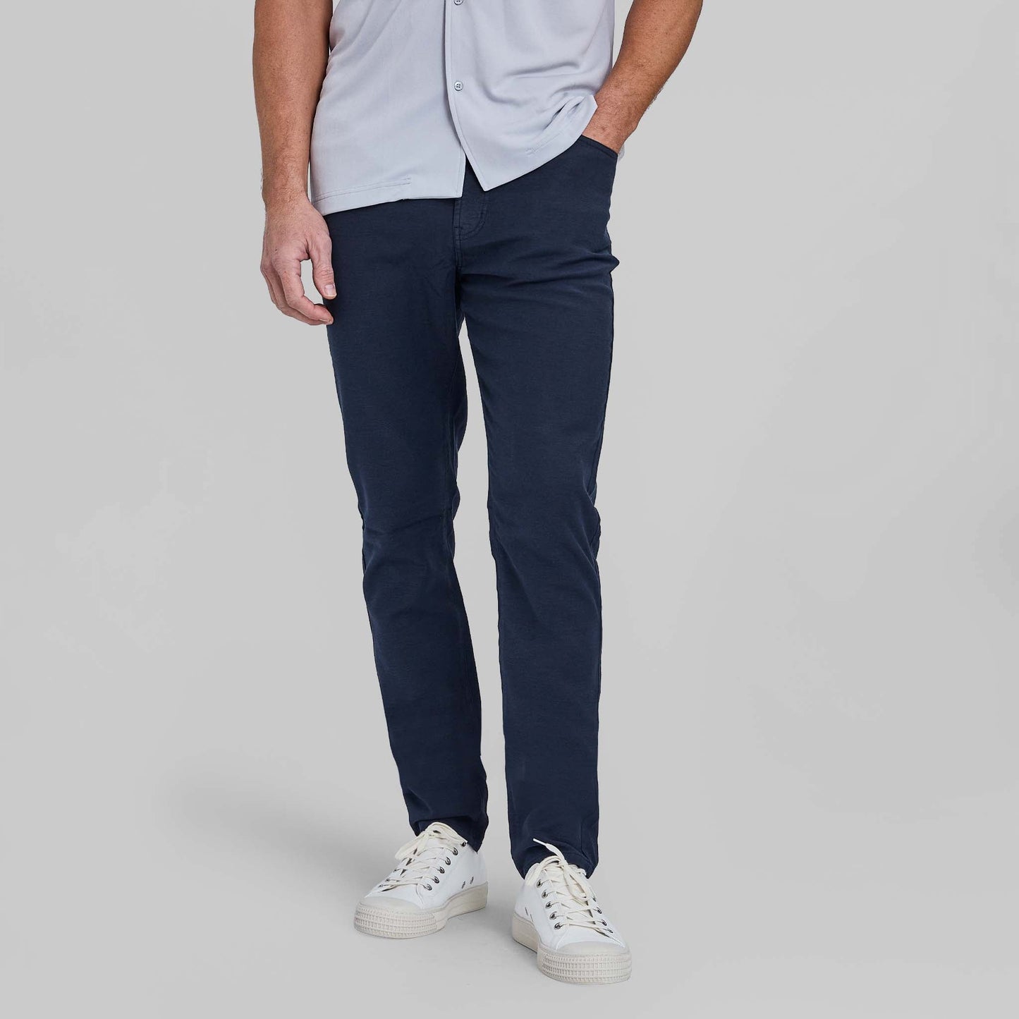 Man wearing navy blue five pocket pants with light blue shirt and white sneakers