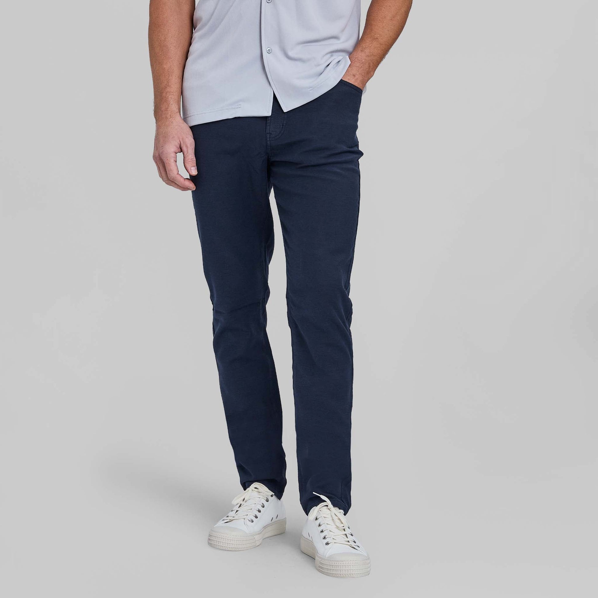 Man wearing navy blue five pocket pants with light blue shirt and white sneakers