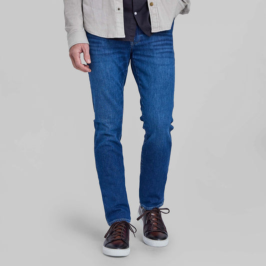 Model wearing medium blue stretch denim jeans with brown leather sneakers