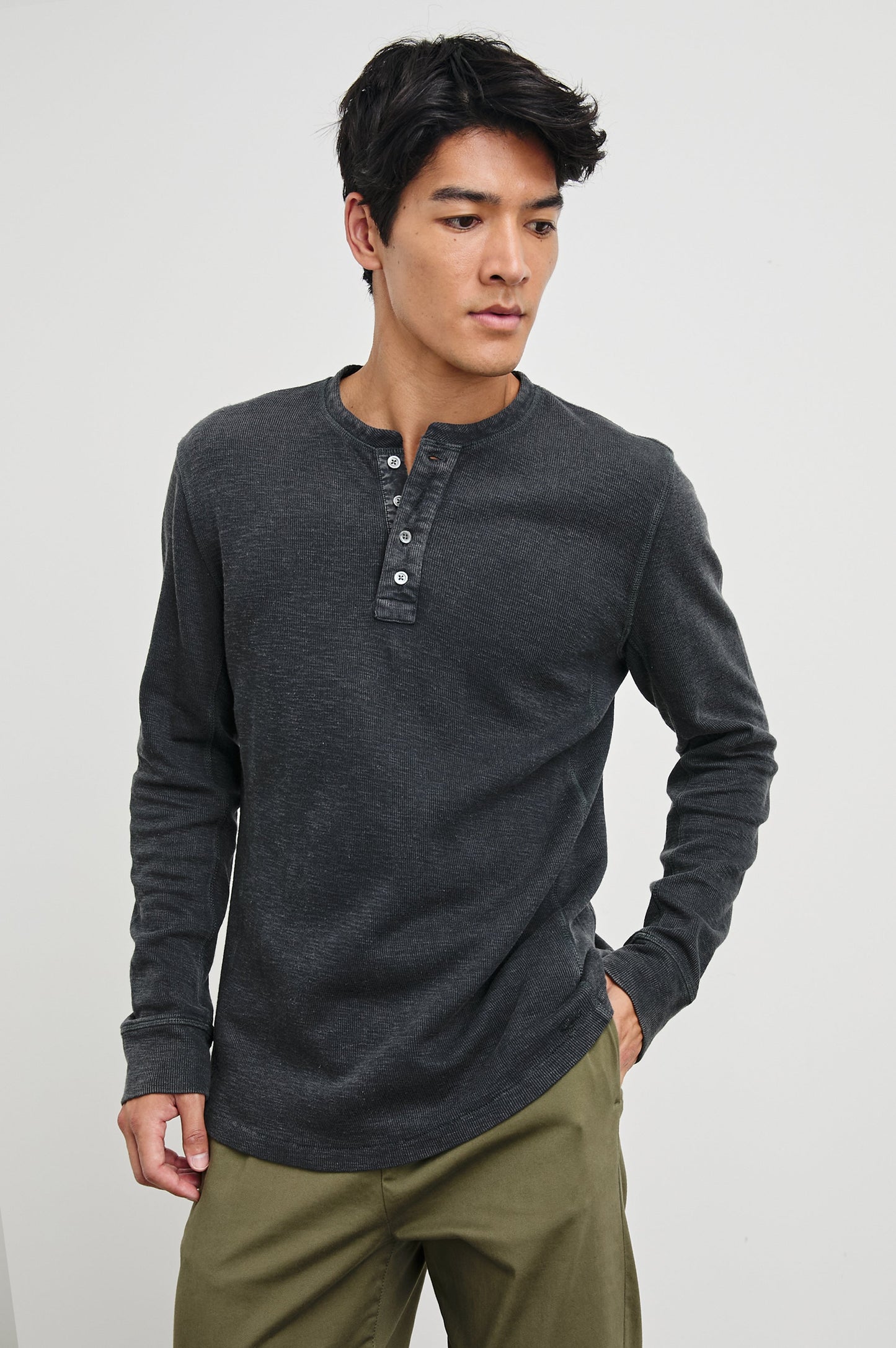 Male model wearing a dark charcoal washed black long-sleeve henley shirt with button placket