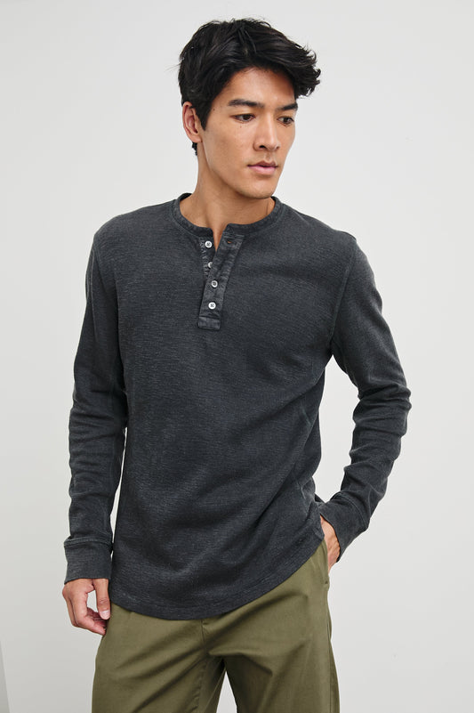 Male model wearing a dark charcoal washed black long-sleeve henley shirt with button placket