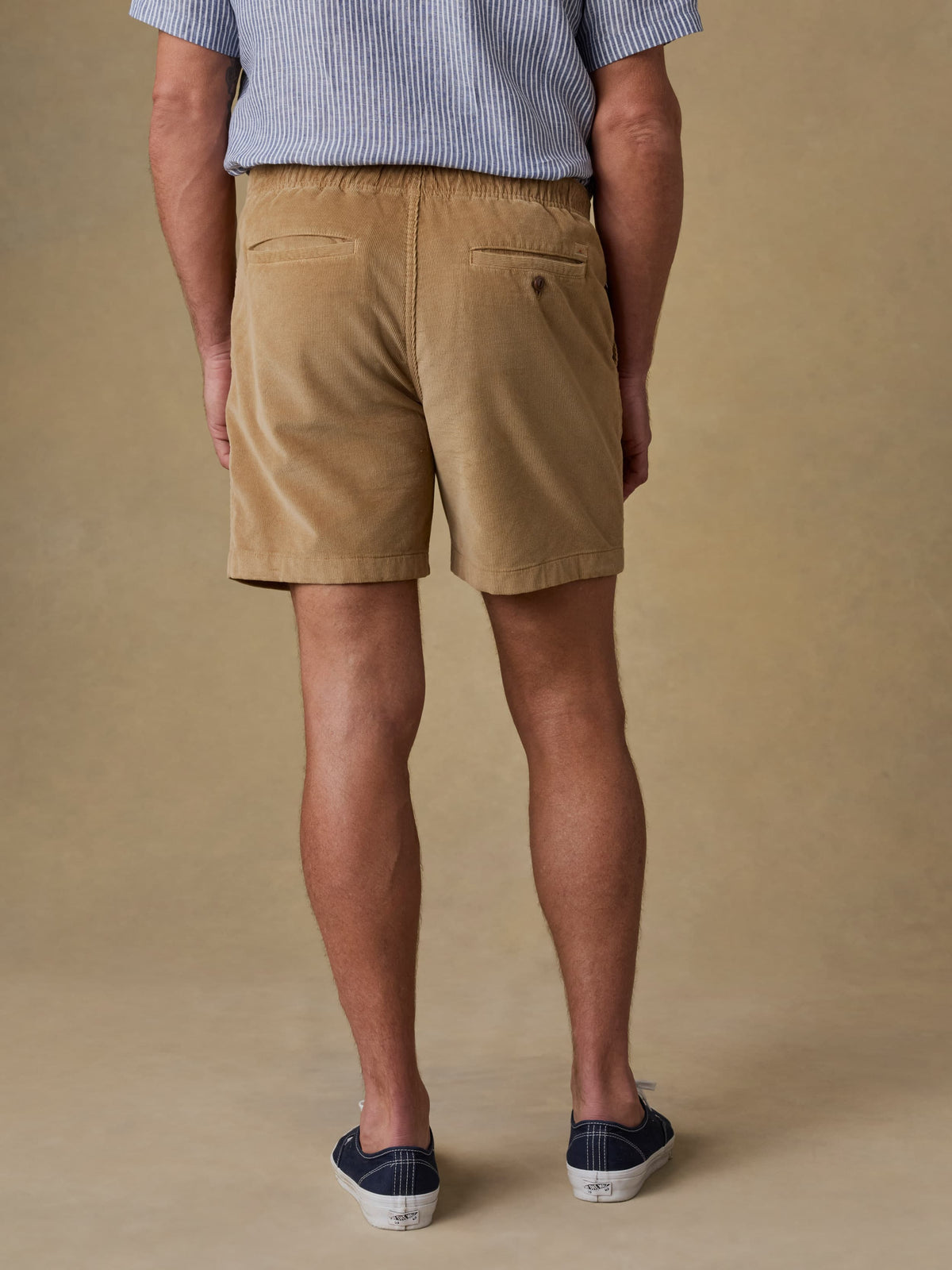Back view of man wearing tan corduroy shorts with striped shirt and canvas shoes