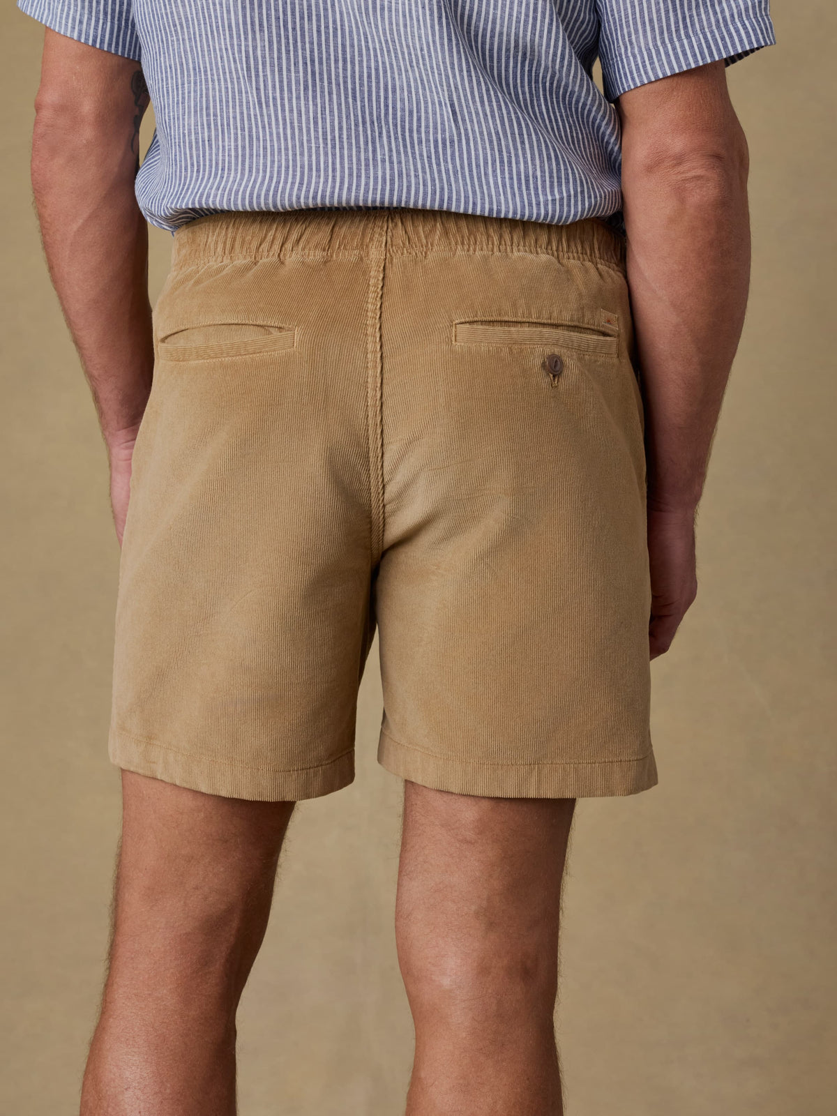 Back view of man wearing tan corduroy shorts with striped shirt