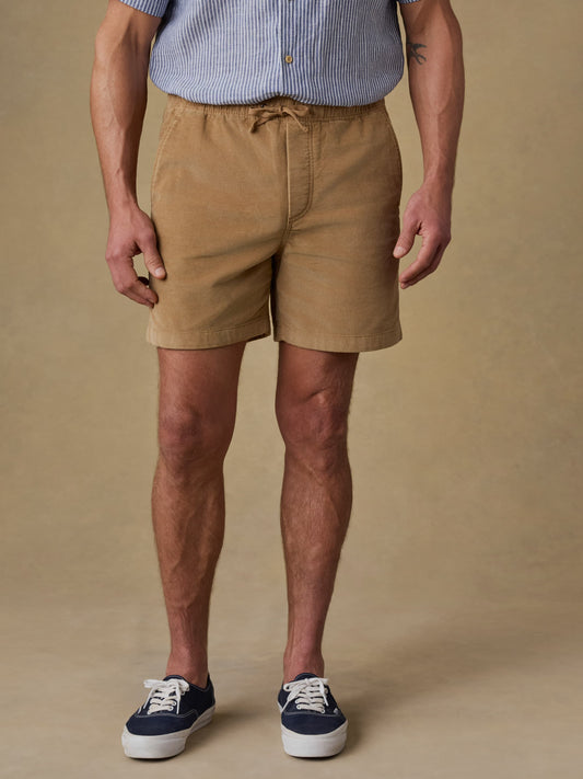 Man wearing tan corduroy shorts with striped shirt and sneakers against beige background