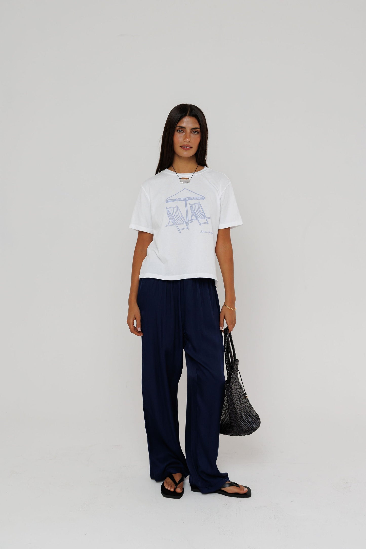 Model wearing white graphic tee with beach chair print and navy wide-leg trousers