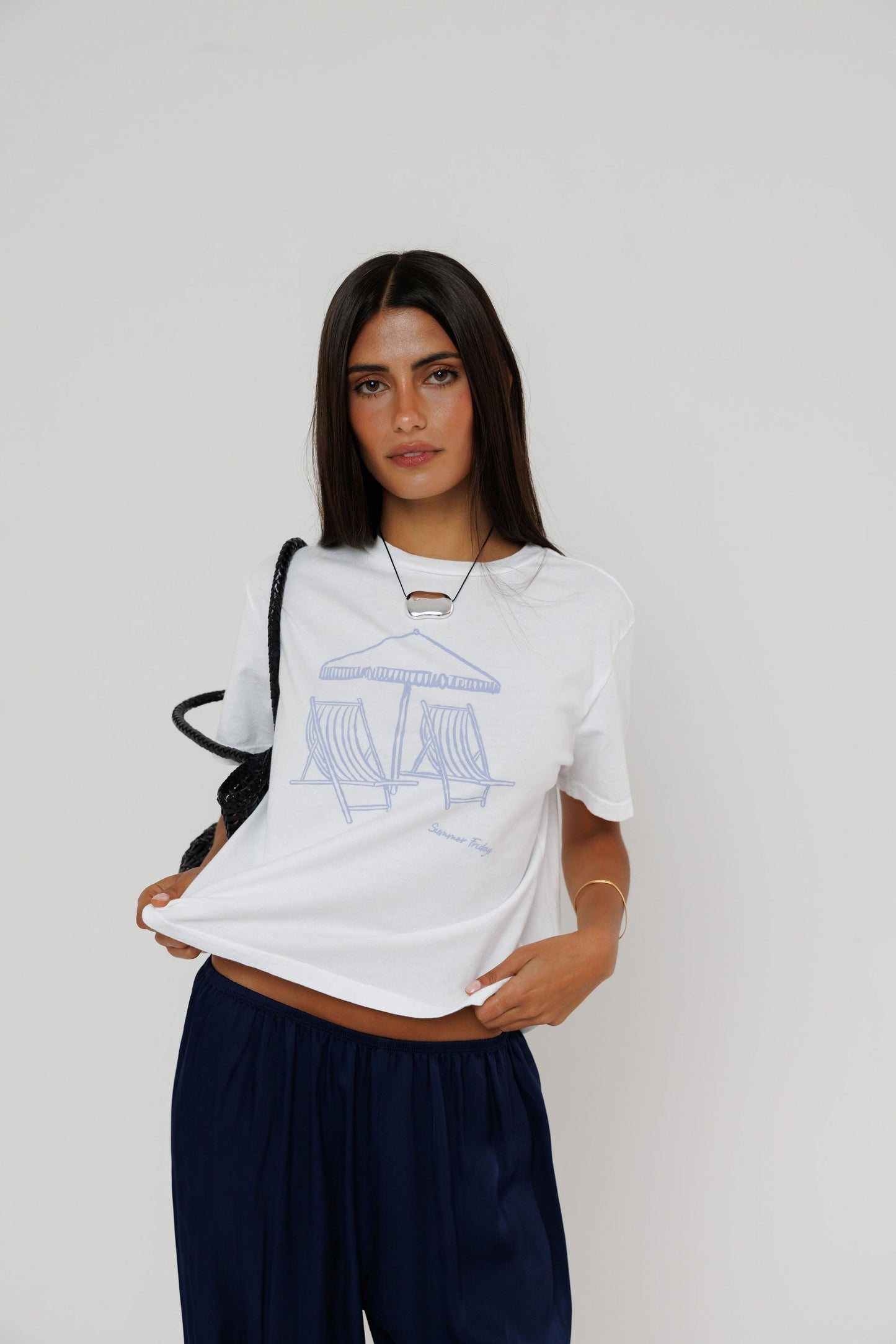 Model wearing white Summer Fridays graphic tee with blue beach chair print and navy pants