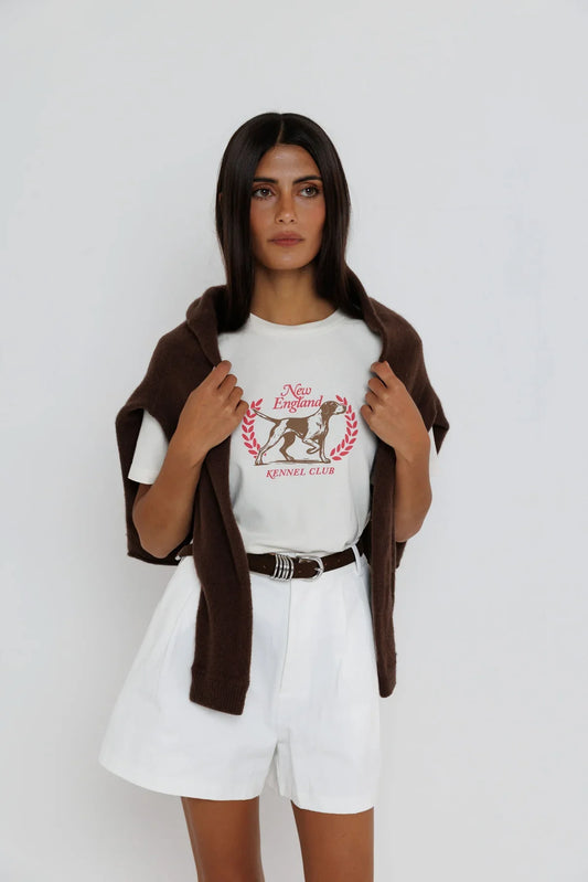 Model wearing white New England Kennel Club graphic tee with brown cardigan and white shorts
