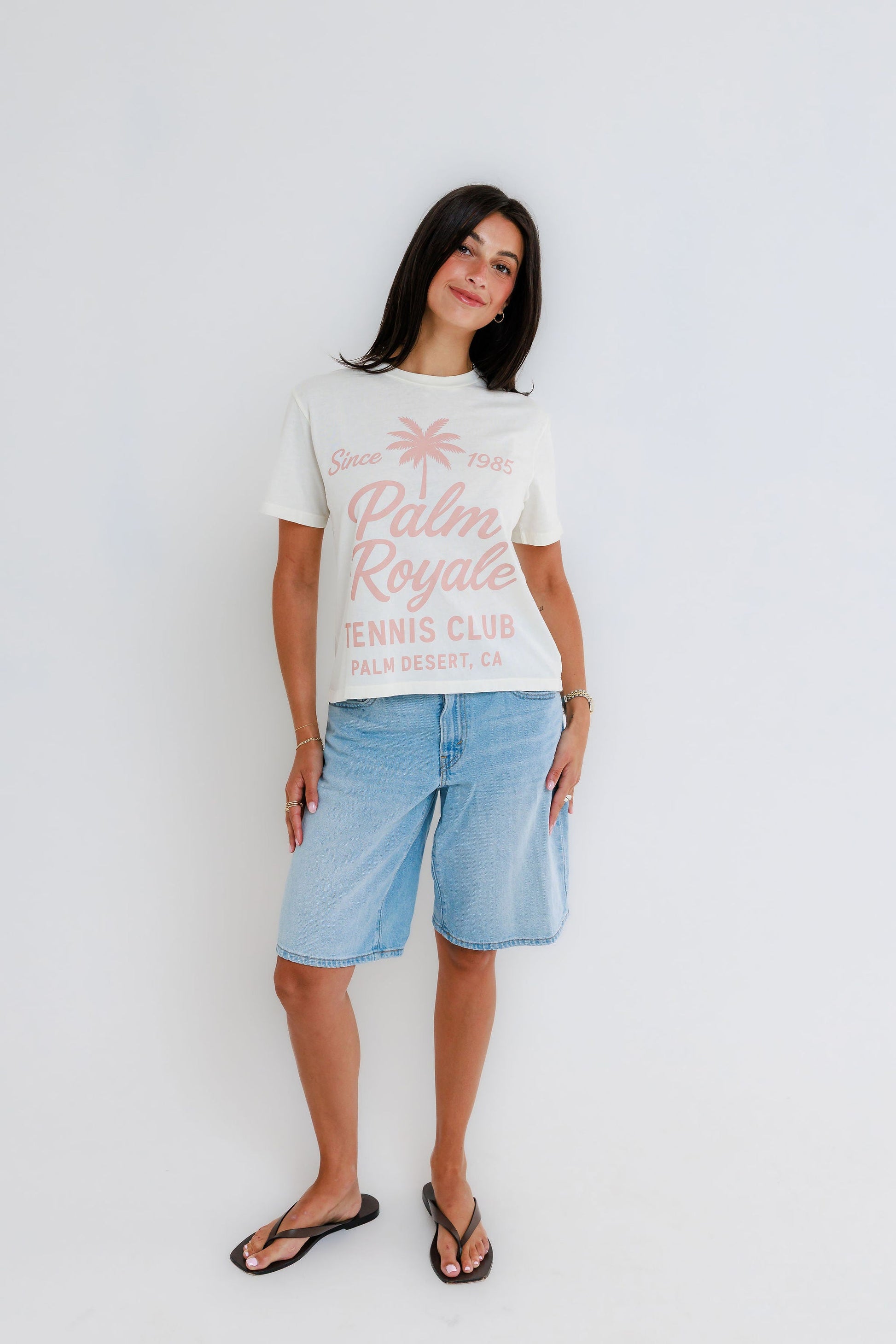 Model wearing cream Palm Royale Tennis Club graphic tee with light wash denim bermuda shorts