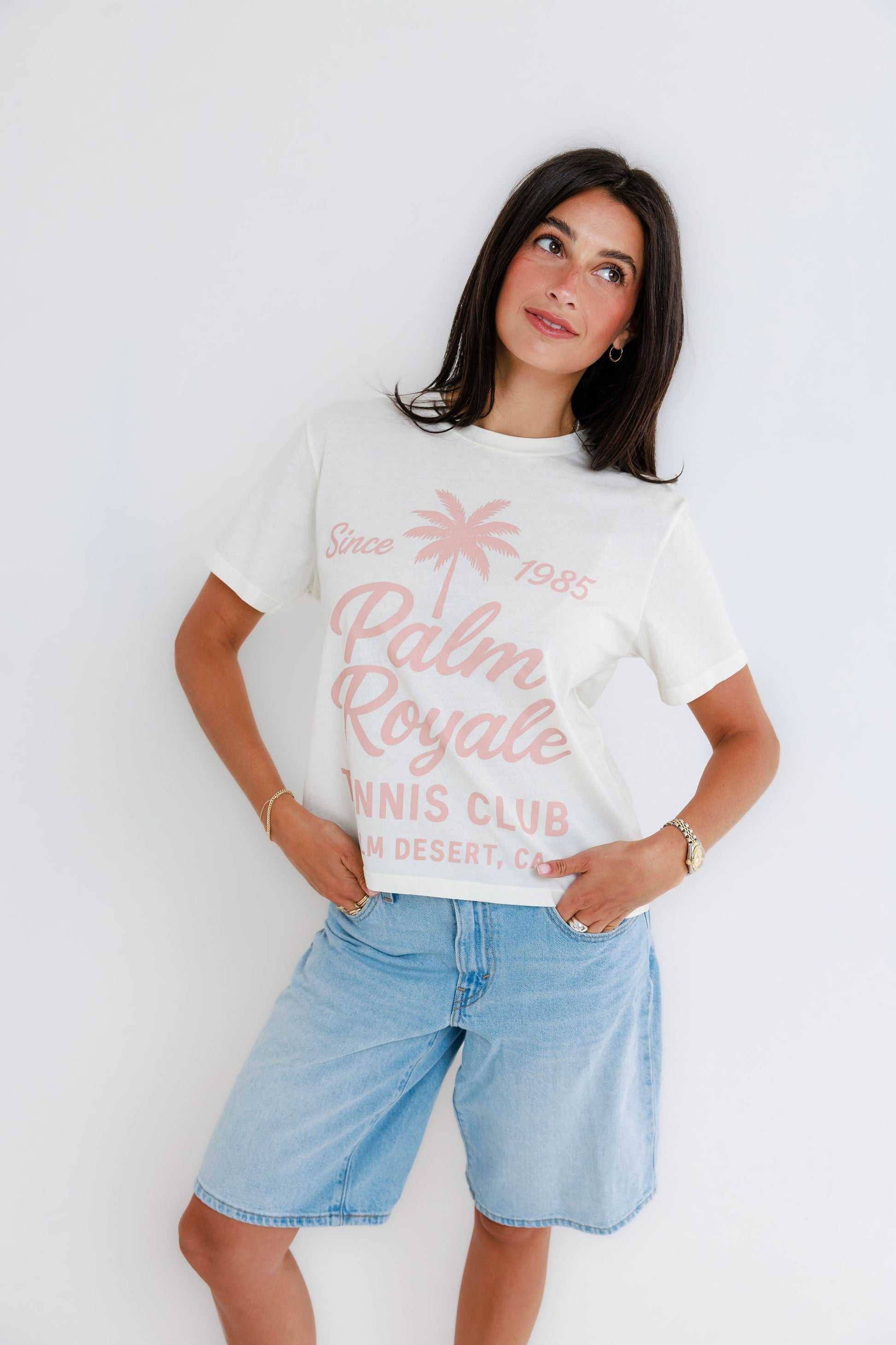 Model wearing white Palm Royale Tennis Club graphic tee with pink print and denim shorts