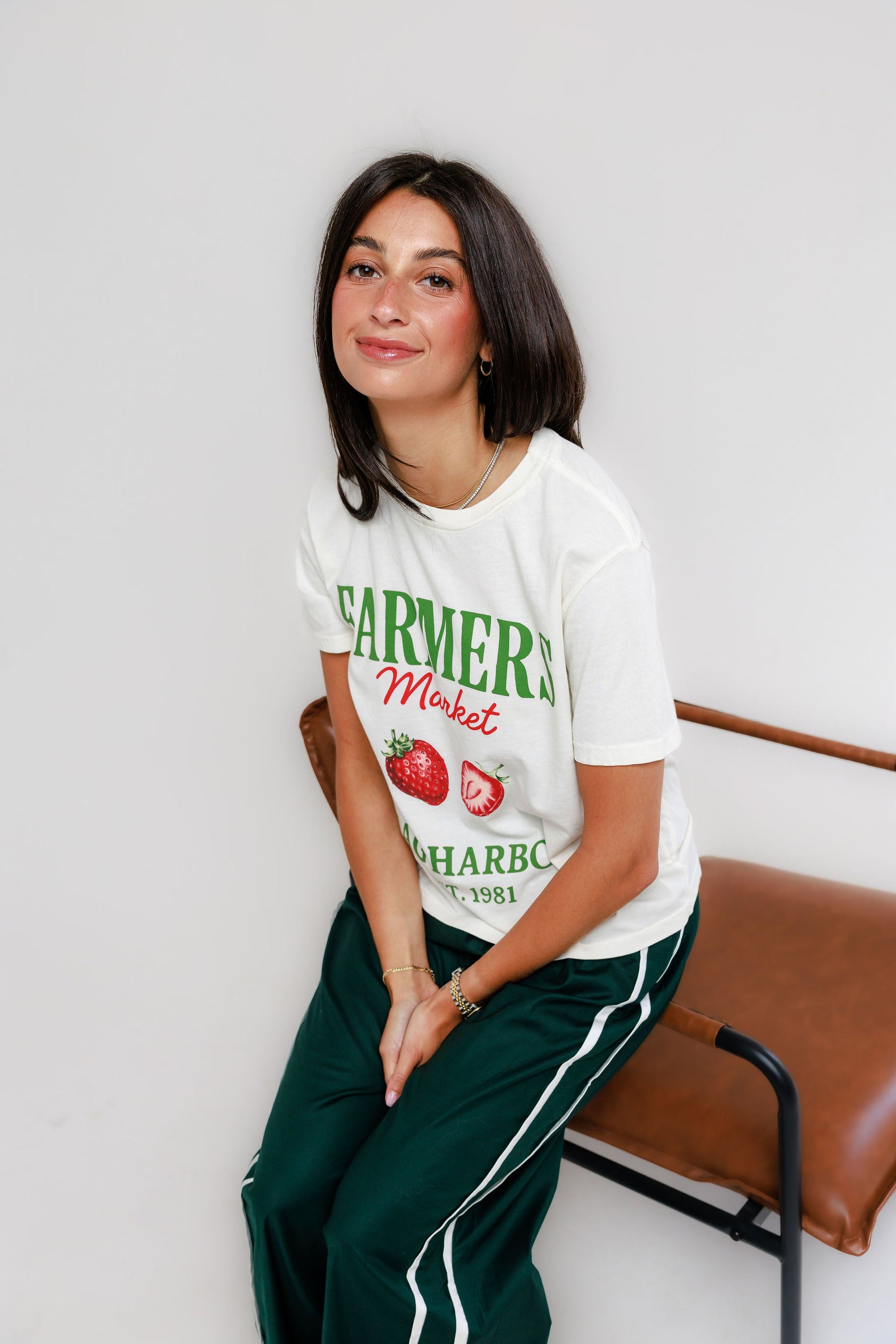Model wearing cream Sag Harbor Farmers Market graphic tee with green track pants