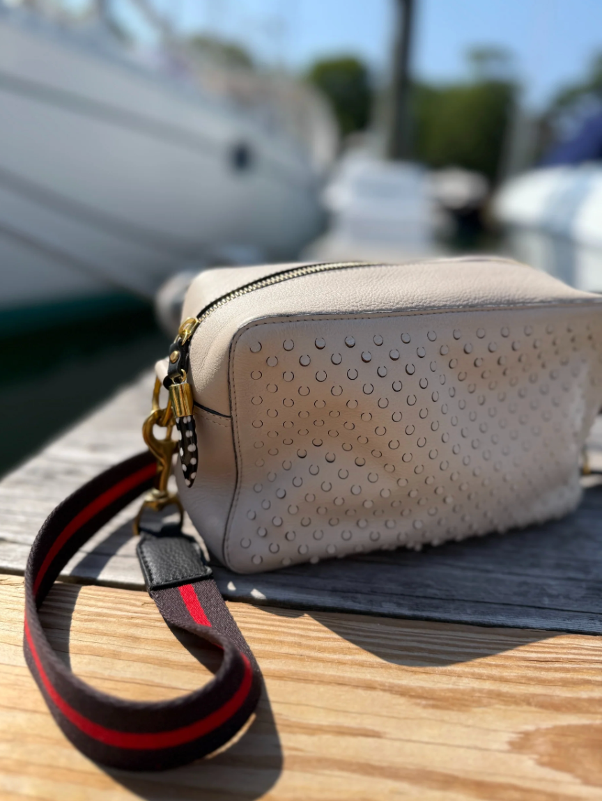 Kempton Amberleigh leather crossbody bag with perforated detailing, gold zipper, and striped strap on wooden dock