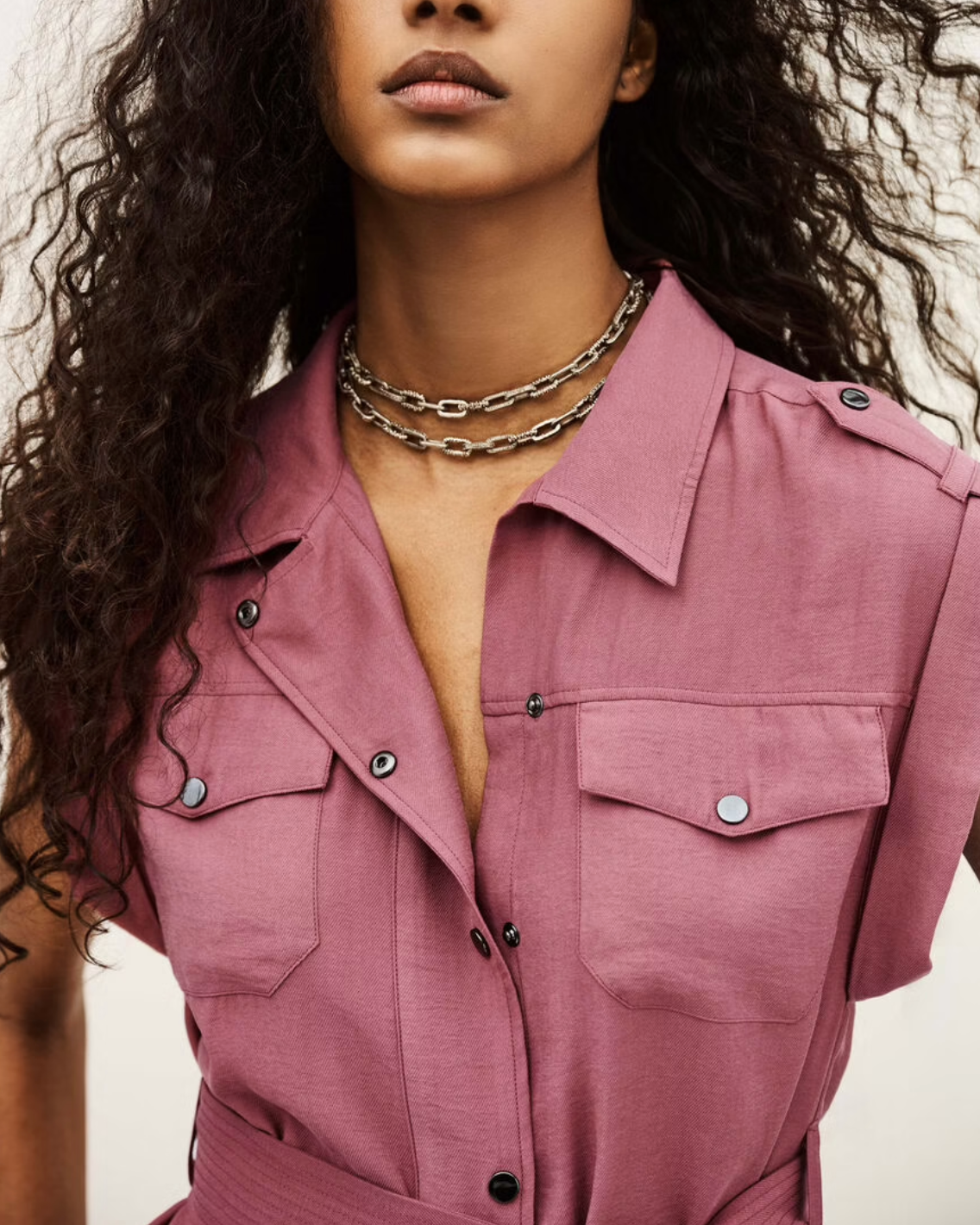 Woman wearing ba&sh pink button-up shirt dress with chest pockets and layered chain necklaces
