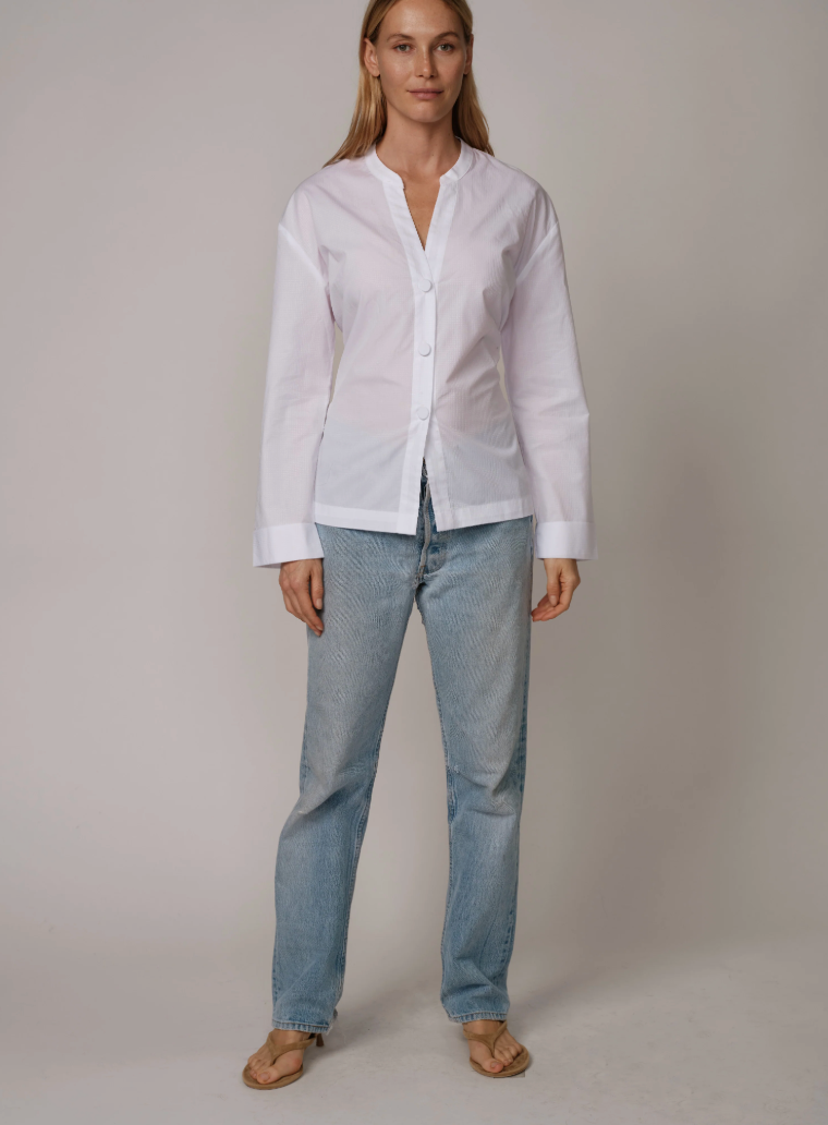 Woman wearing Cissa white button-up shirt with bow back detail and light blue jeans, standing against neutral background.