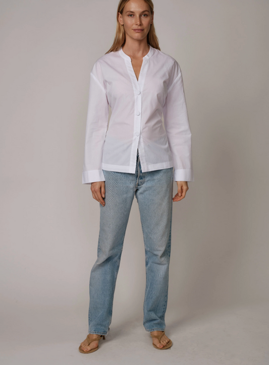 Woman wearing Cissa white button-up shirt with bow back detail and light blue jeans, standing against neutral background.