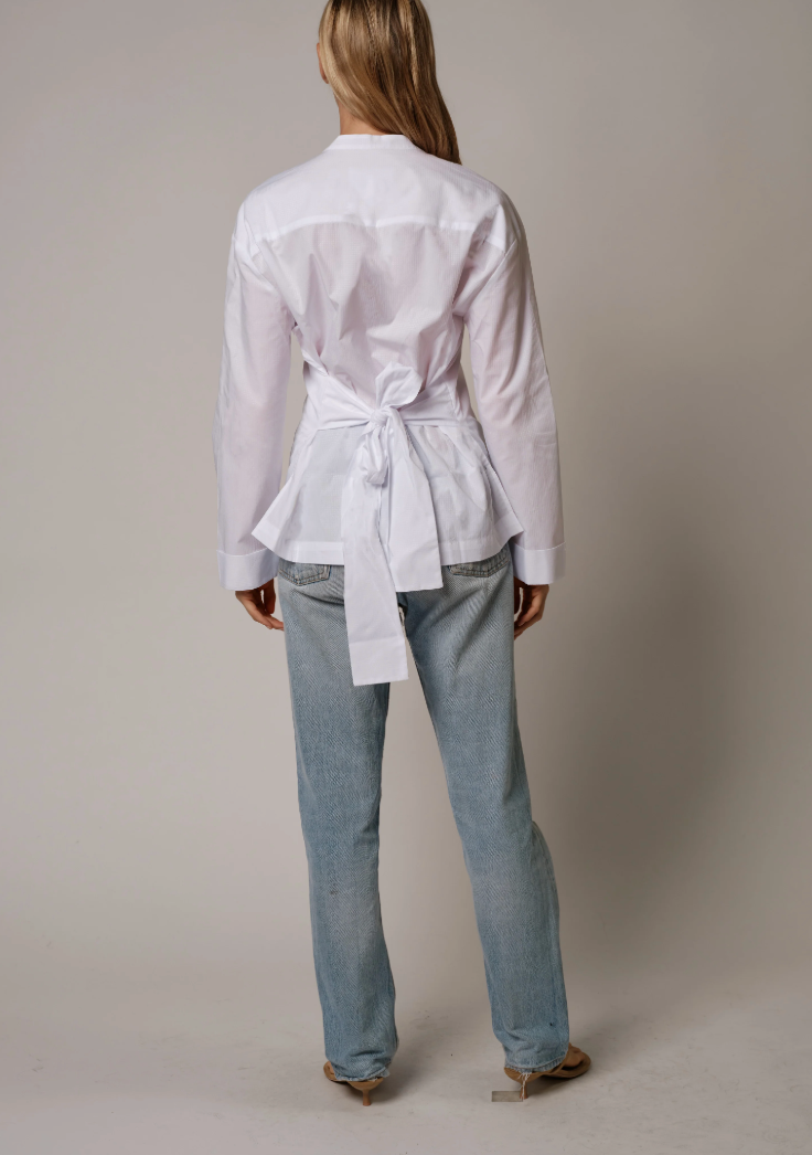 Back view of woman wearing Cissa white button-up shirt with bow tie detail and light wash jeans.