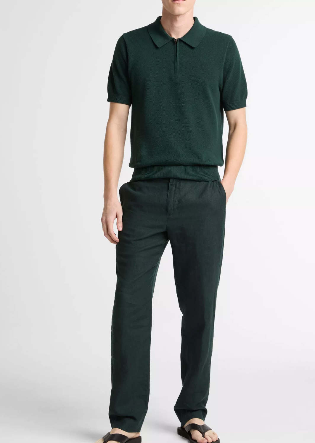 Man wearing Vince short-sleeve zip polo shirt in dark green with matching relaxed-fit trousers and sandals.